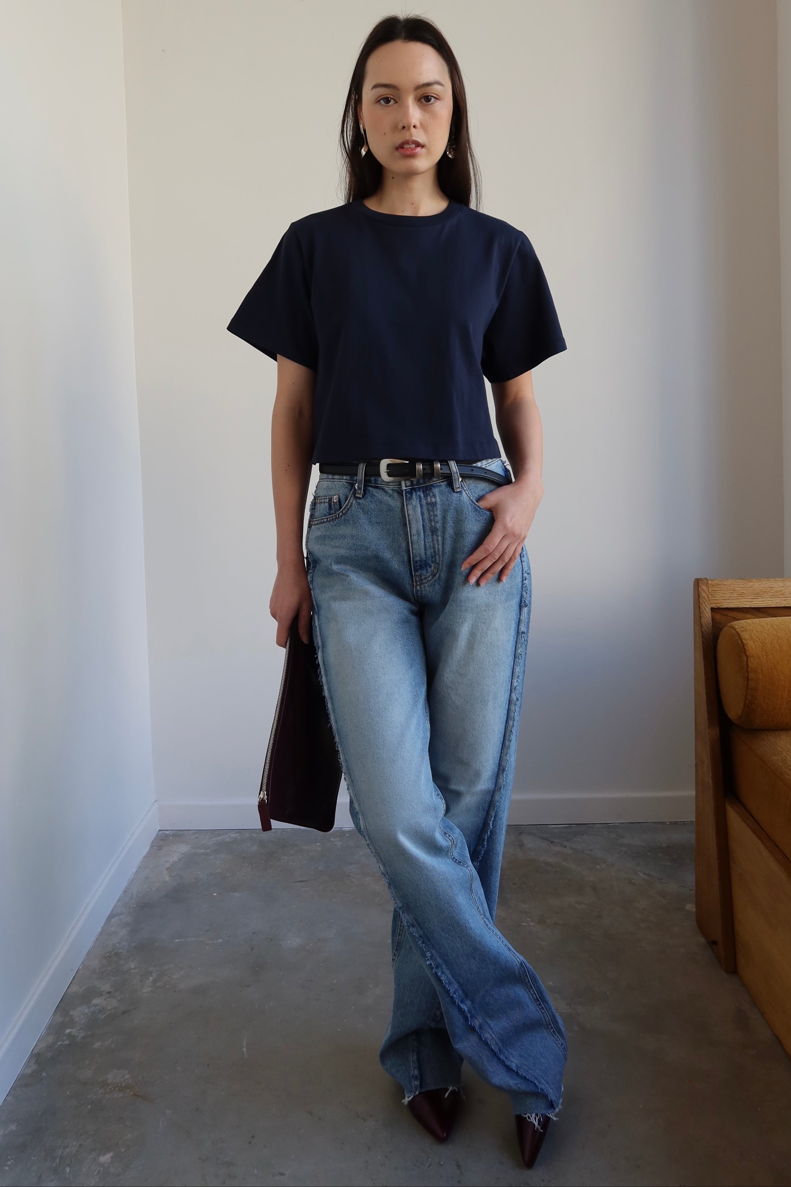 Person wearing a black t-shirt and blue jeans standing in a minimalistic room.