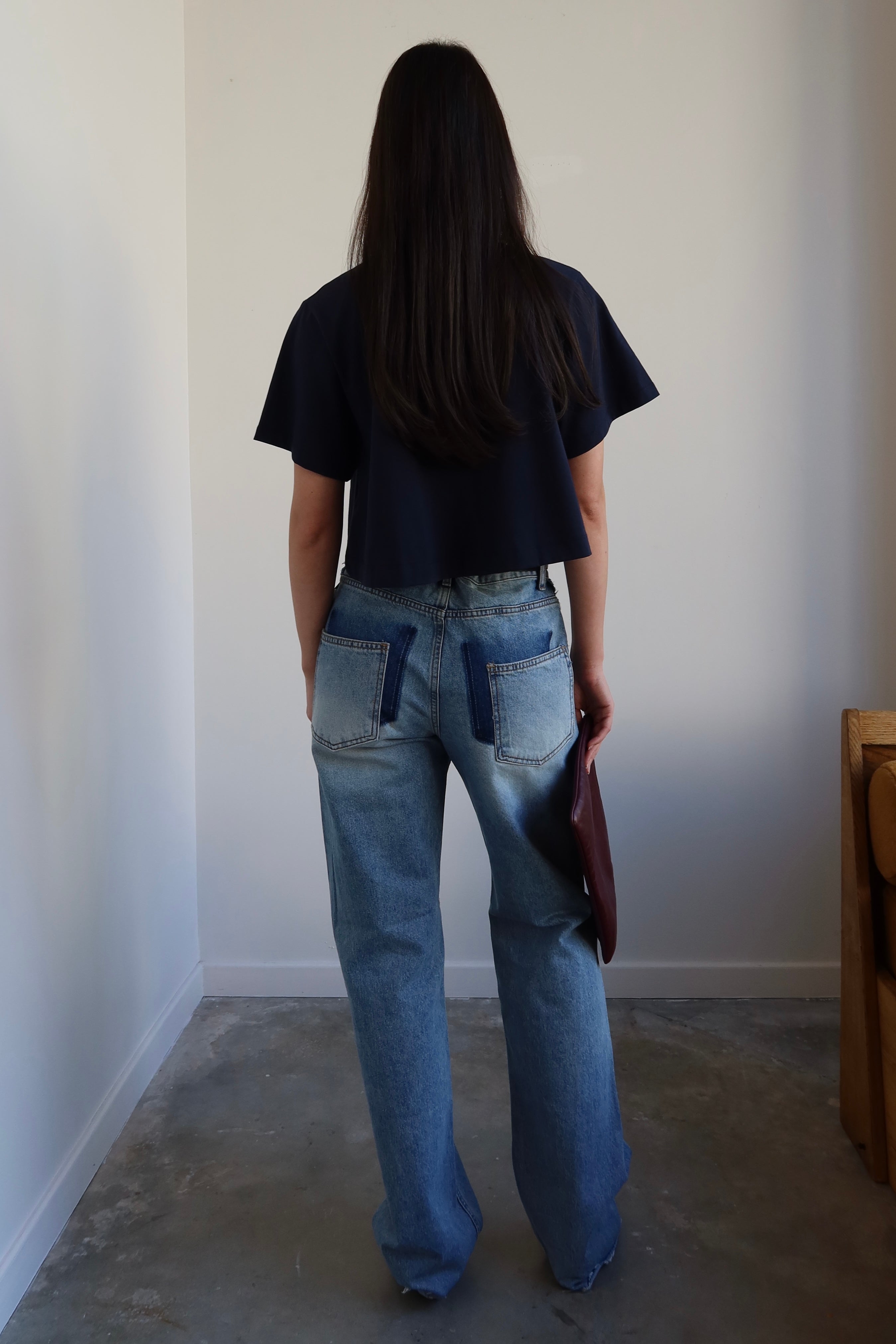 Person wearing a black t-shirt and blue jeans standing in a minimalistic room.