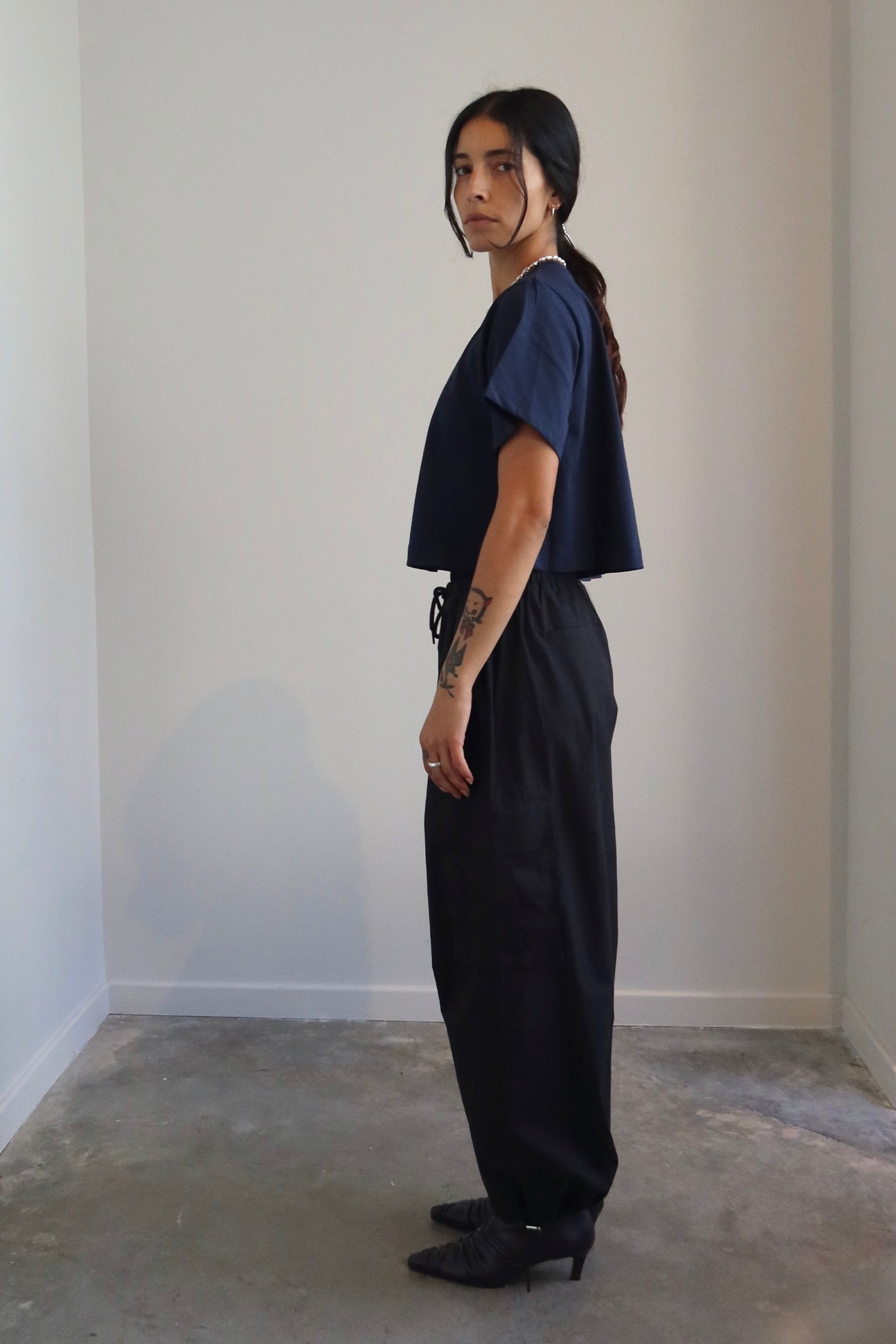 A person wearing a navy relaxed fit cropped t-shirt paired with black trousers.