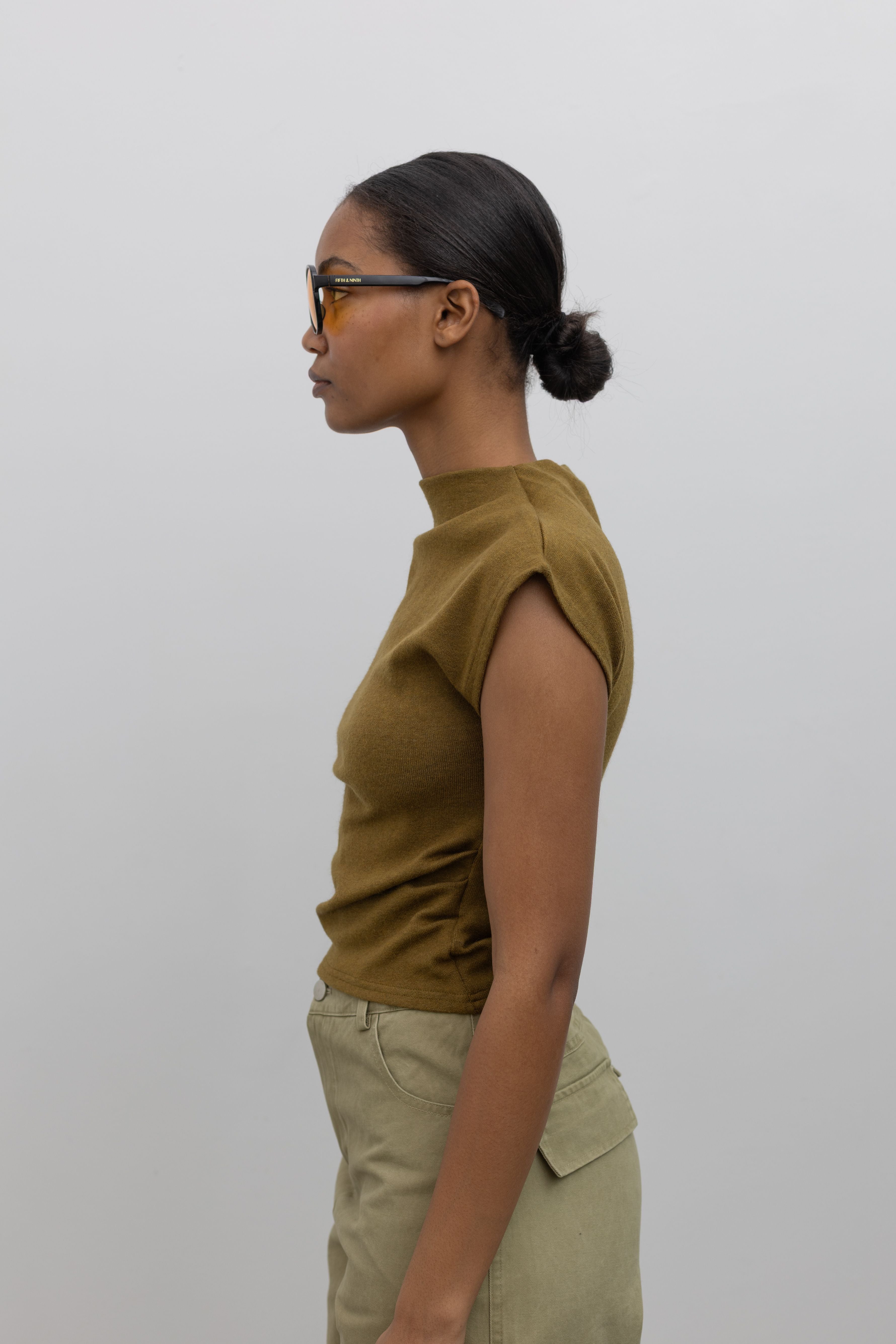 Close-up side view of a woman wearing Contemporary fashion in a Alas Eius label olive mock neck knit slim fit top with flattering cap sleeves at Alas Eius