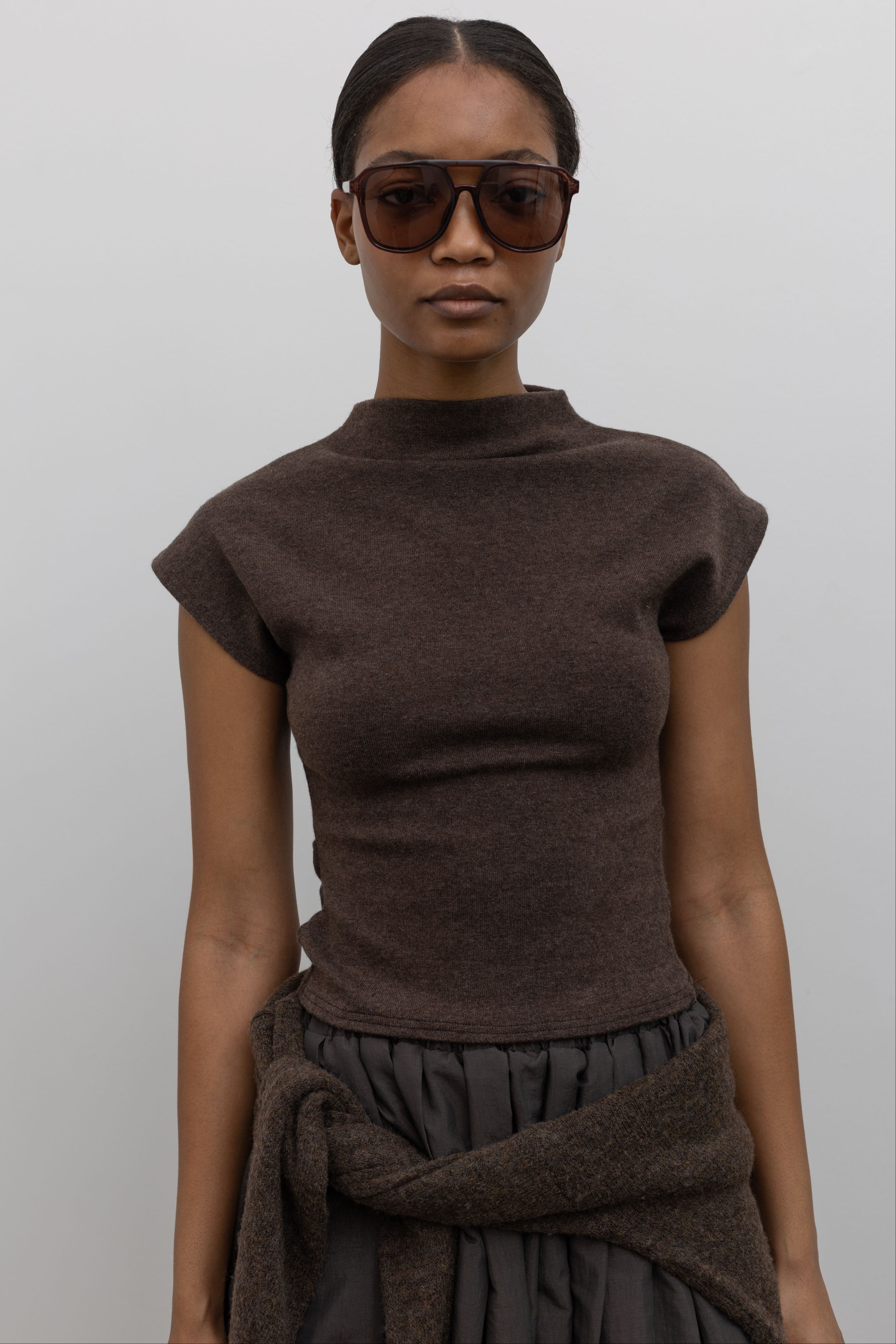 Close-up front view of a woman wearing Contemporary fashion in a Alas Eius label brown mock neck knit slim fit top with flattering cap sleeves at Alas Eius