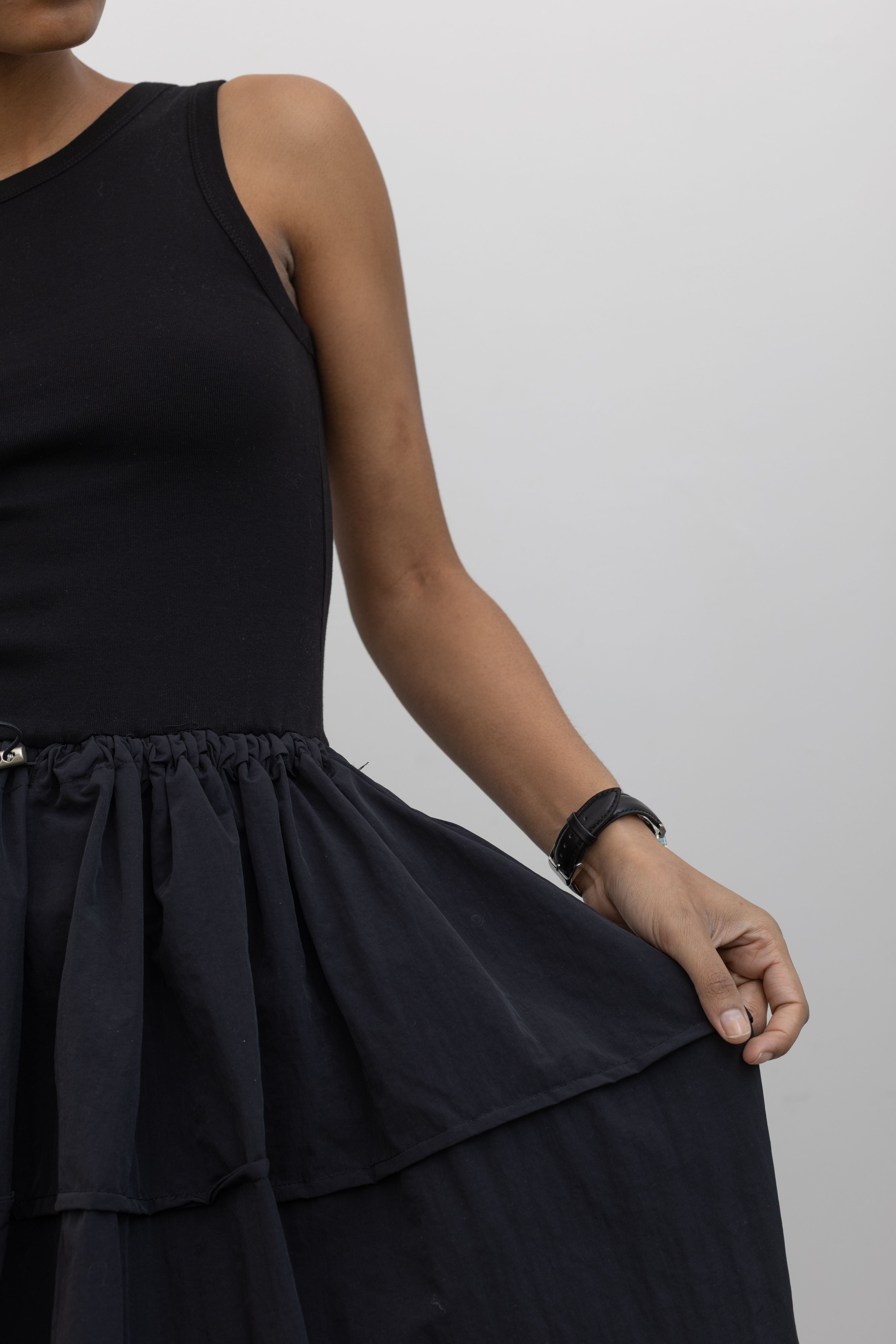 Detailed product view of Woman wearing Spring fashion in a flattering Alas Eius brand dress with a cotton bodice and a structured nylon skirt cinched by an adjustable drawstring waist paired with black Salomon sneakers and sunglasses at Alas Eius 