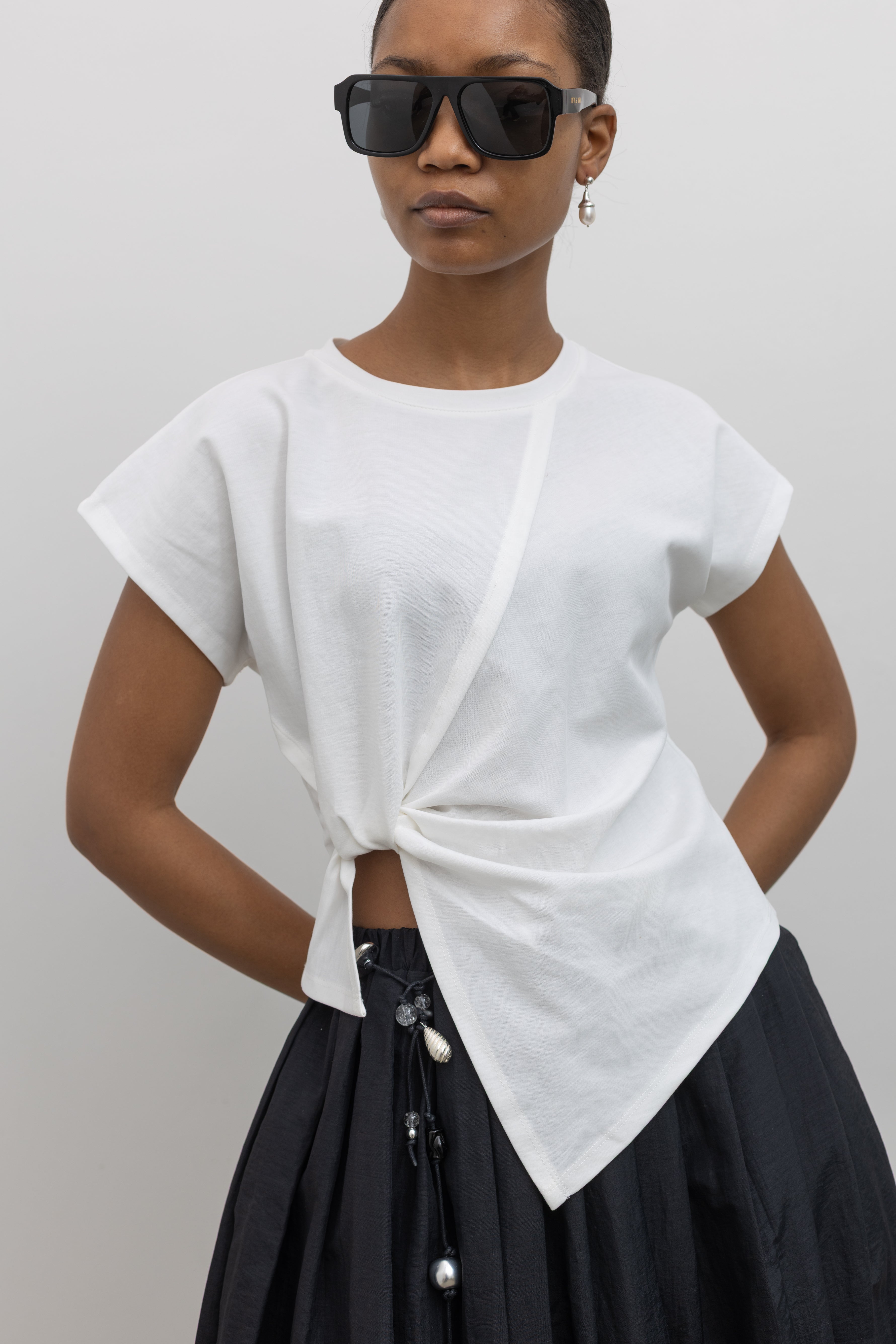 Woman wearing a white top with a knot detail and black pleated skirt with beaded belt at alas eius