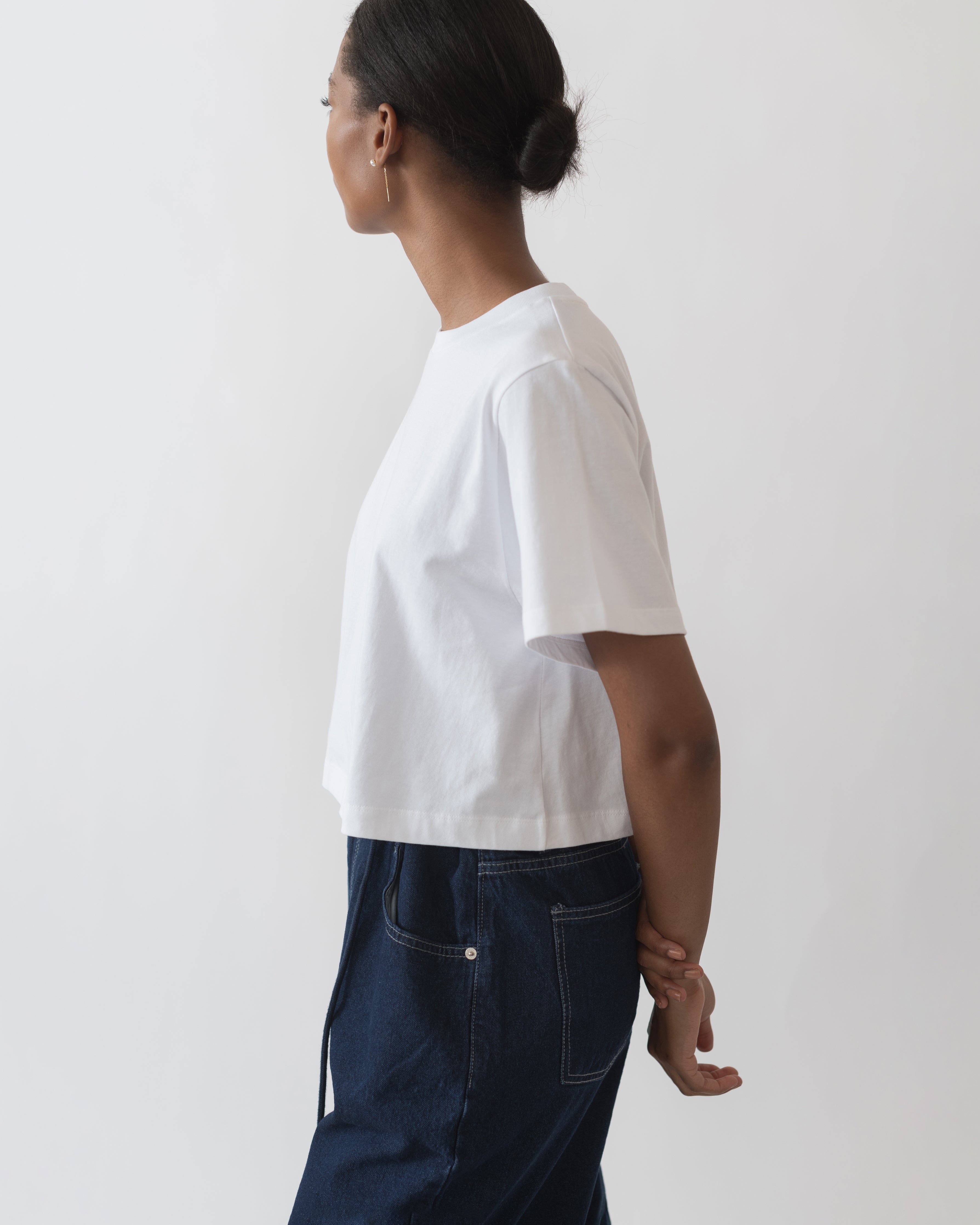 A person wearing a white relaxed fit cropped t-shirt, looking to the side.