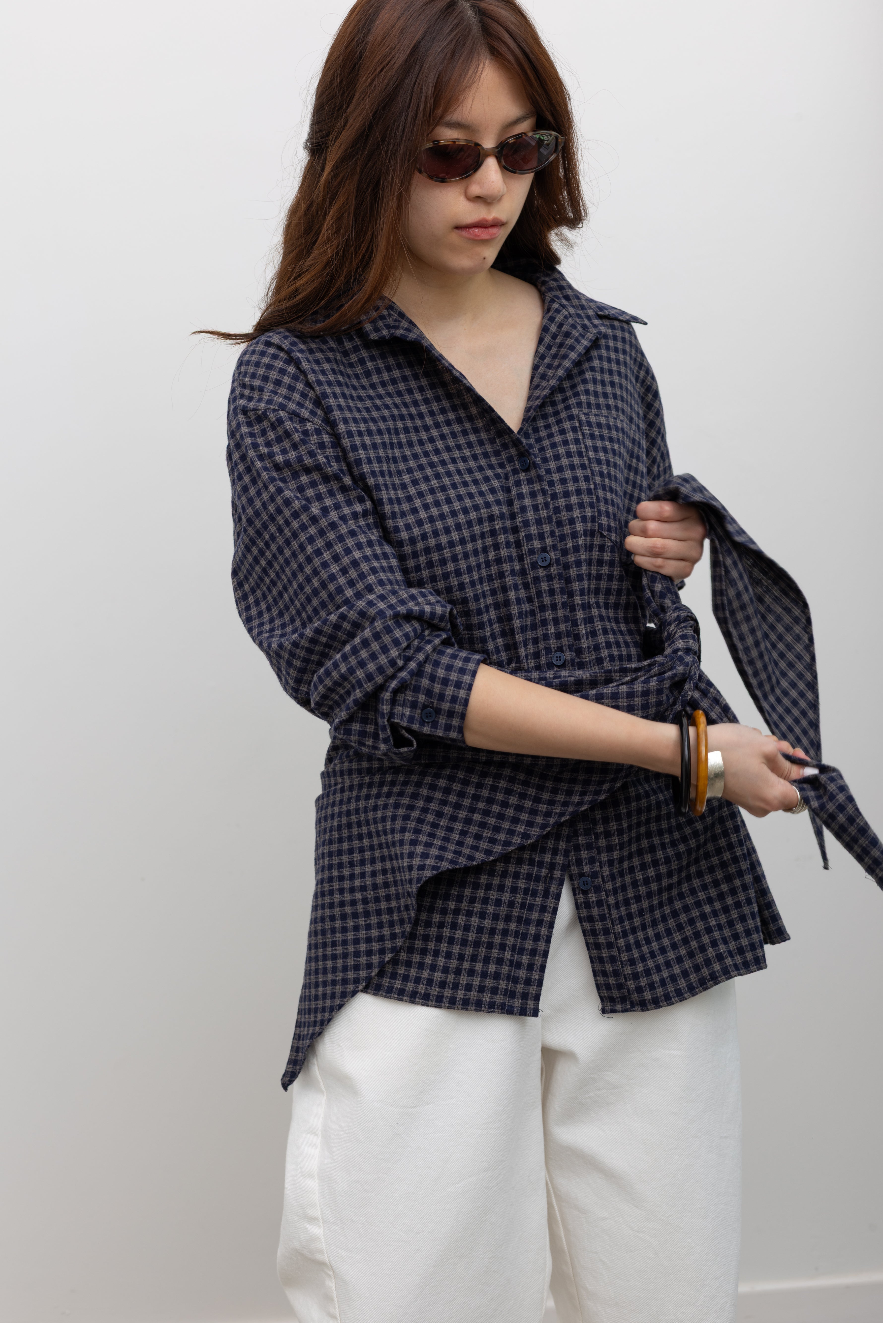 Alas Eius label women's oversized navy blue and tan plaid button-down shirt styled with coordinating bandana scarf around waist for a flattering cinched look paired with white denim jeans at Alas Eius. 