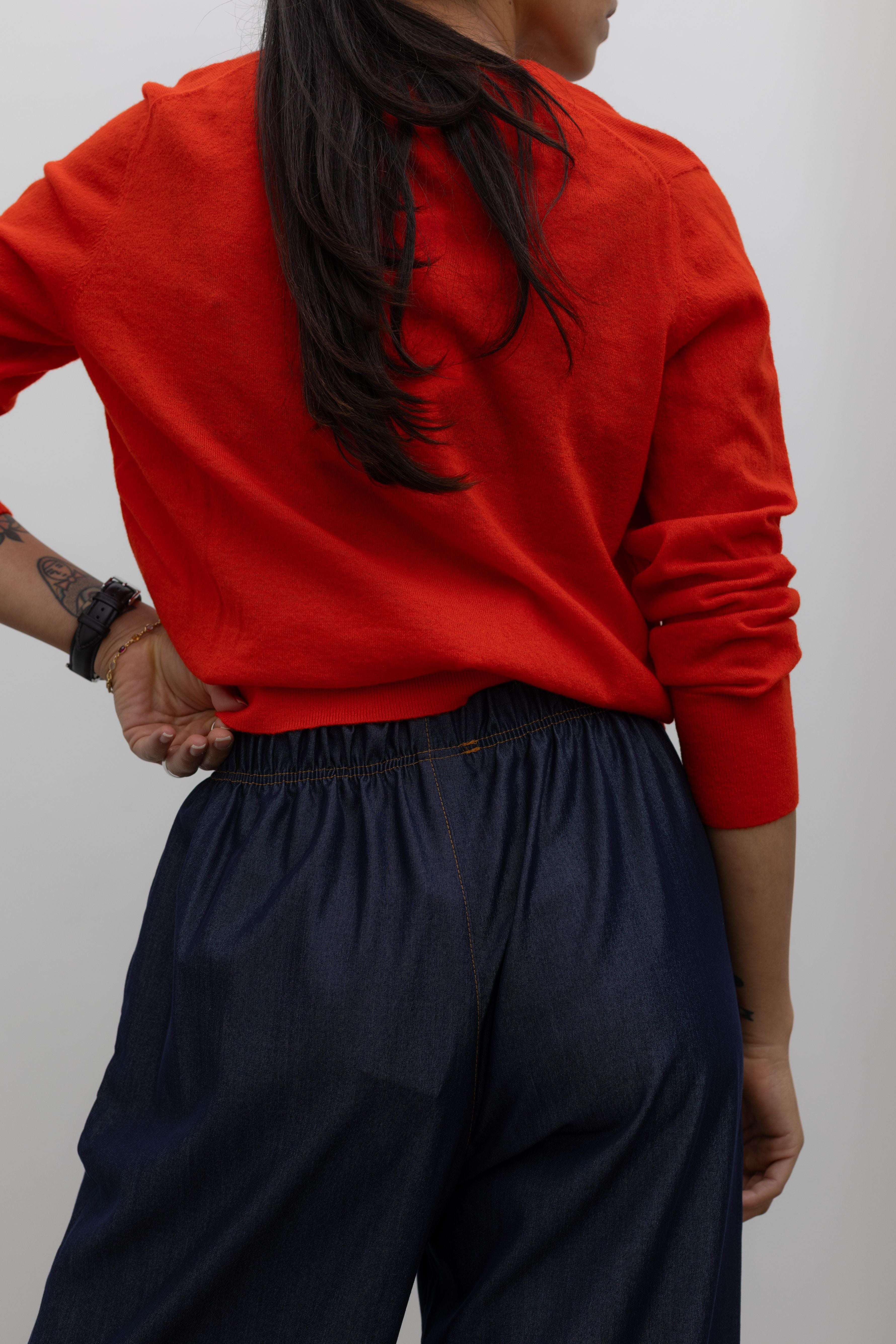 Detailed product back view of a Woman standing wearing an everyday outfit with a Tibi Red v-neck cashmere sweater and Alas Eius Label Tencel Blend Dark Wash Tailored Wide Leg Pull On Pants Alas Eius. 