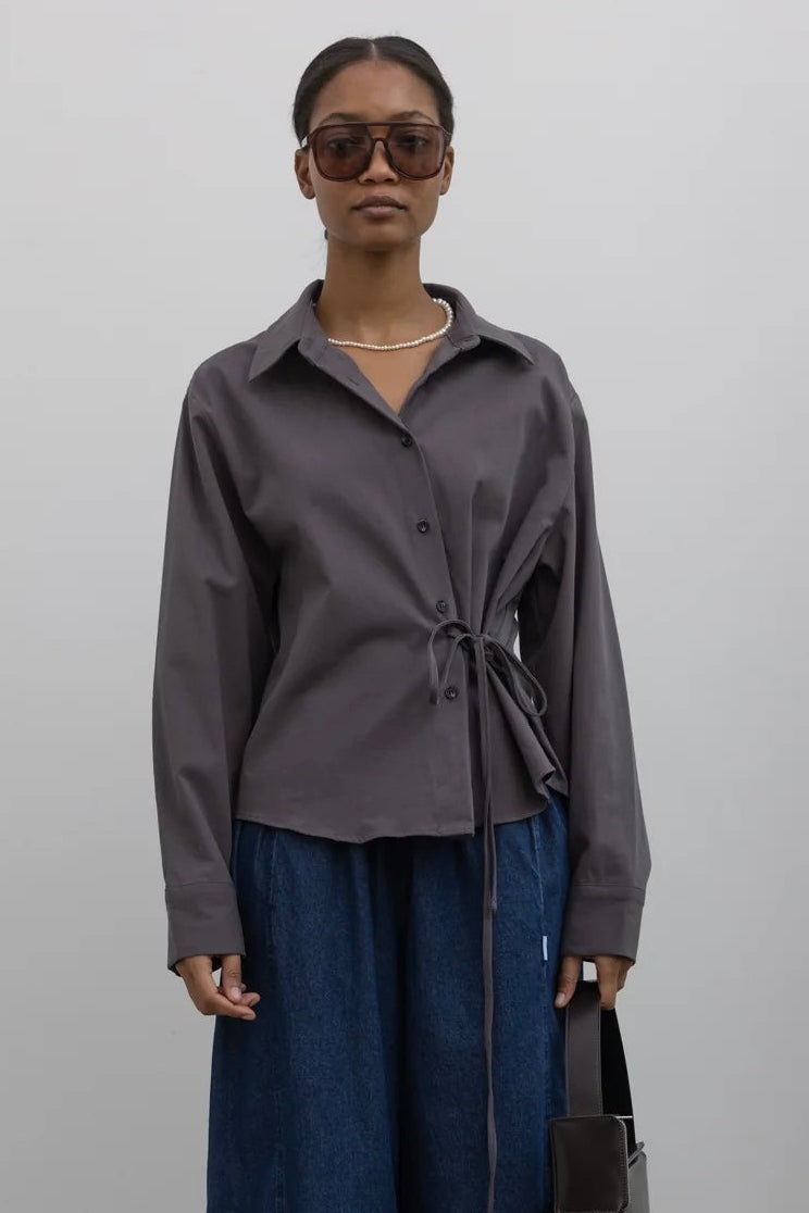 Woman wearing everyday capsule wardrobe essential in a modern and sculptural Alas Eius label brushed cotton cinched waist button down collared long sleeve top with denim and accessories at Alas Eius