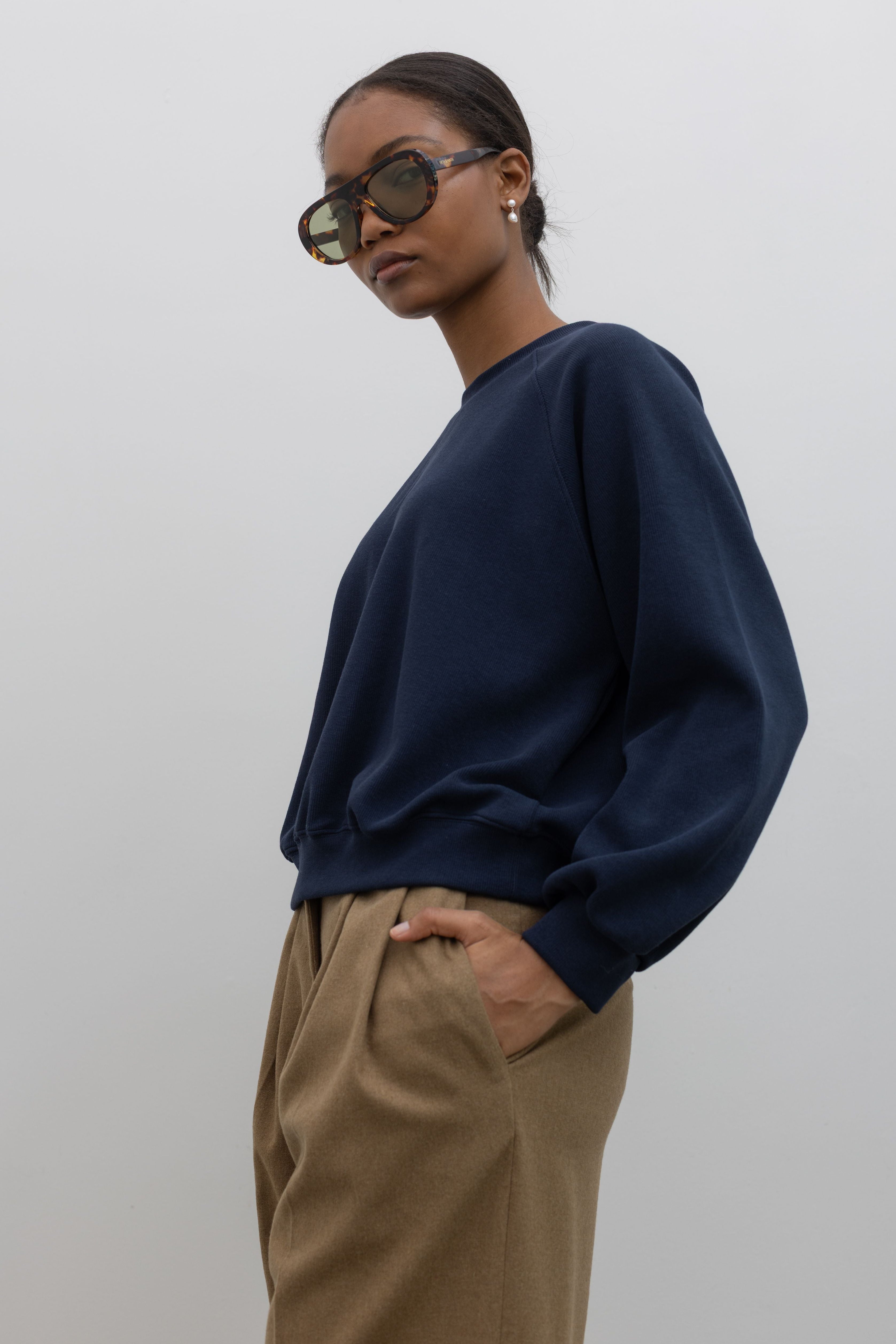 Person wearing a navy blue sweater and beige pants against a white background