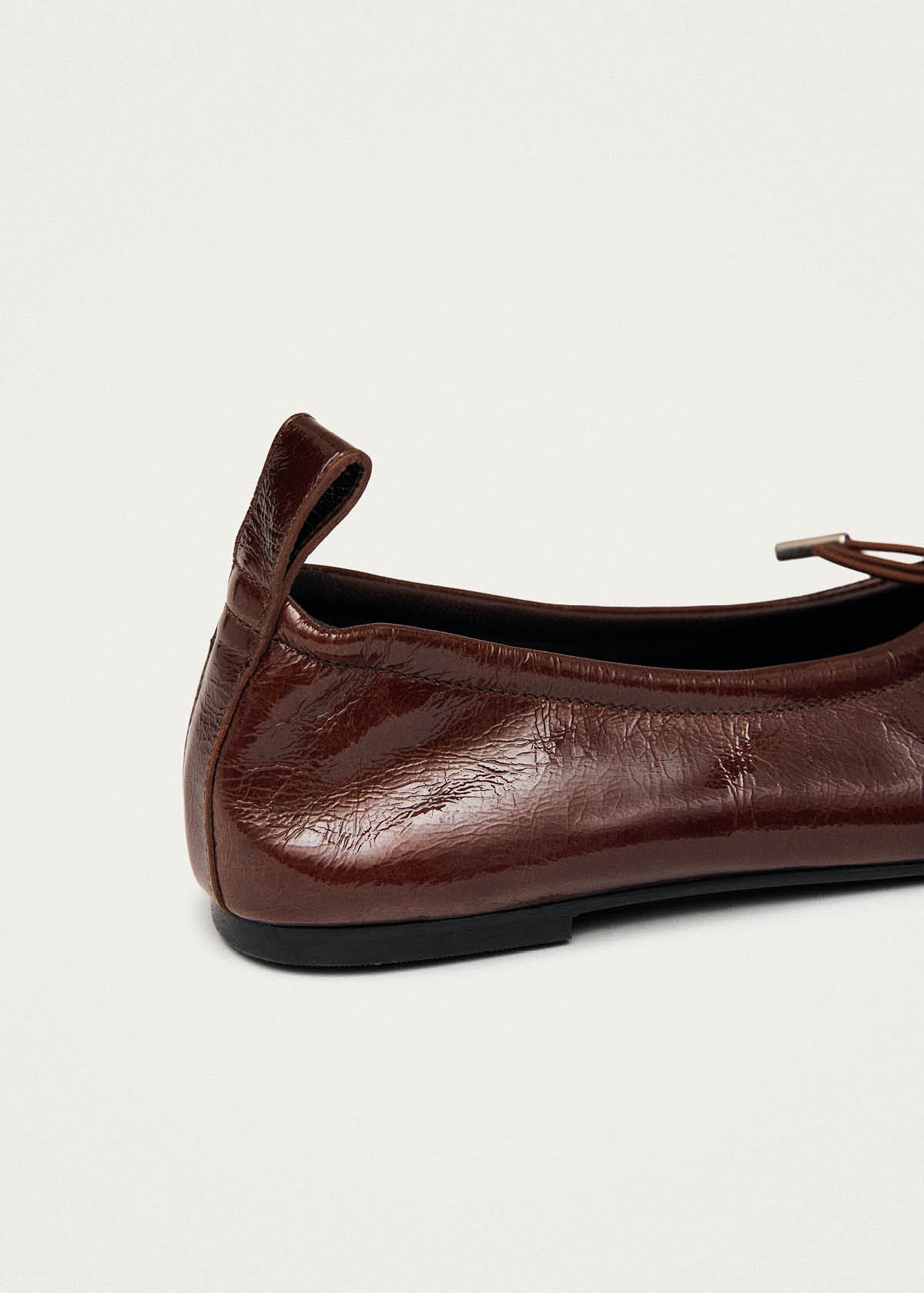 Close-up of Alohas brown patent leather ballet flat showing elasticized back and flexible sole construction at Alas Eius