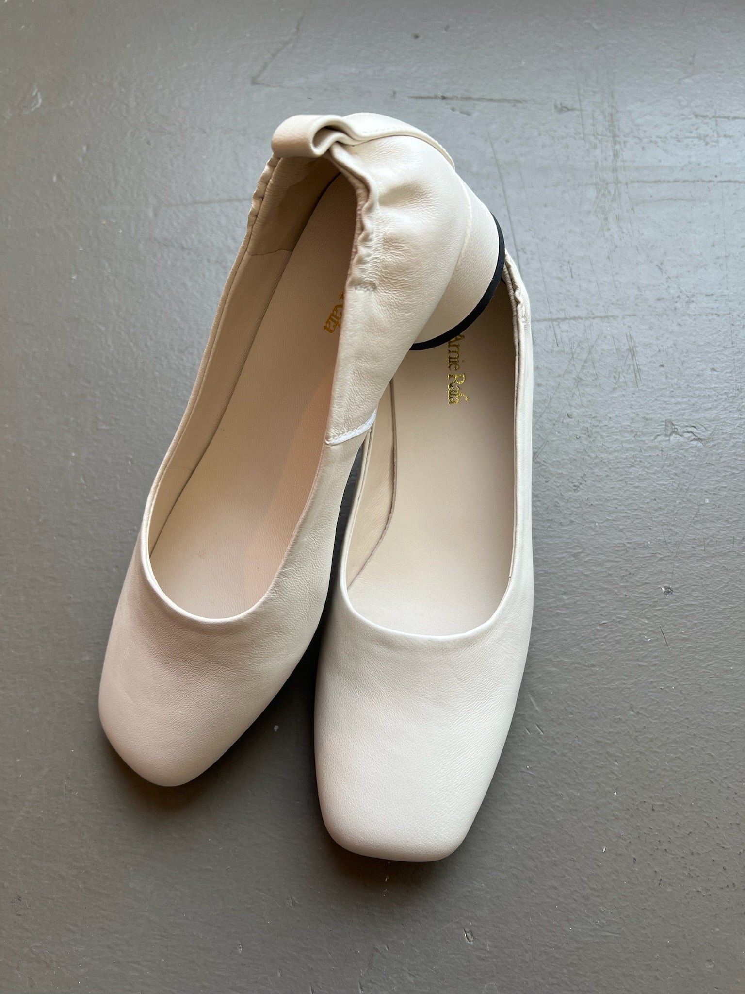 A pair of feminine and modest Amie Rafa label white leather rounded block heel glove pumps with a modern squared off toe and elastic ruched back at an Alas Eius store. 