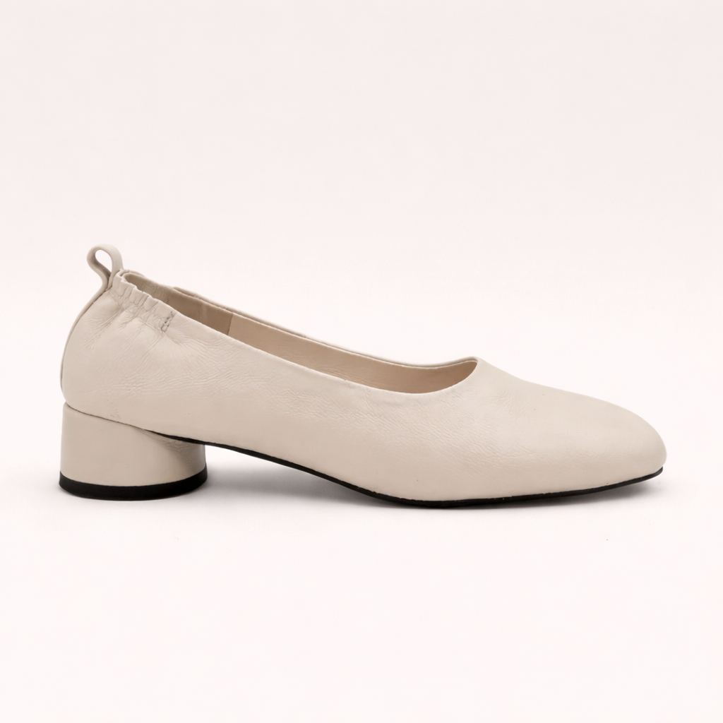 Side view of the modern and sculptural Amie Rafa label white leather rounded block heel glove pumps with a modern squared off toe and elastic ruched back at an Alas Eius store. 