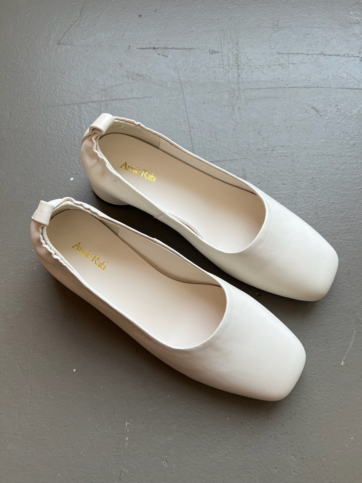 Aerial view of the feminine and sculptural Amie Rafa label white leather rounded block heel glove pumps with a modern squared off toe and elastic ruched back at an Alas Eius store. 