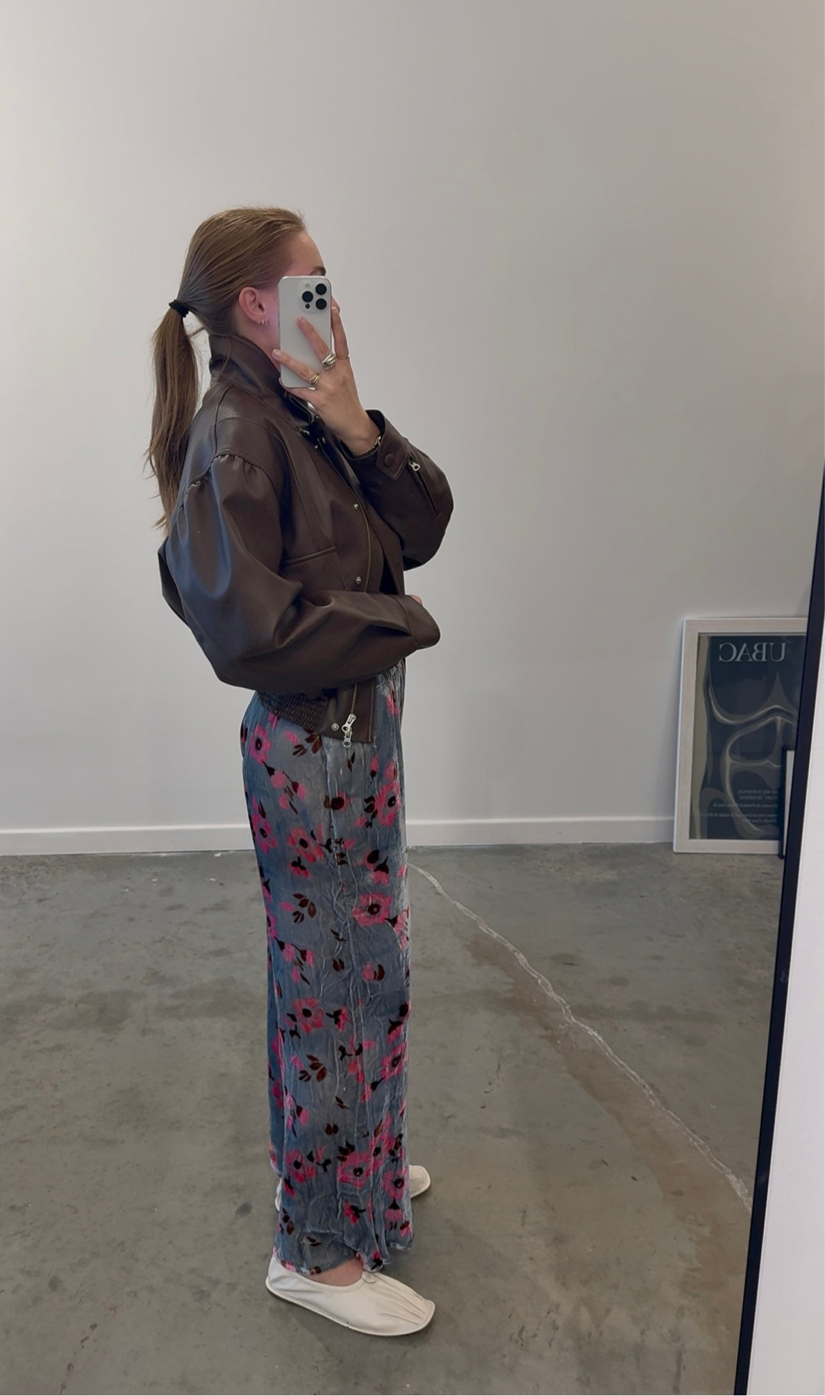 Side view of a woman wearing a brown leather jacket paired with Anntian silver and pink floral velvet wide leg pants at Alas Eius.