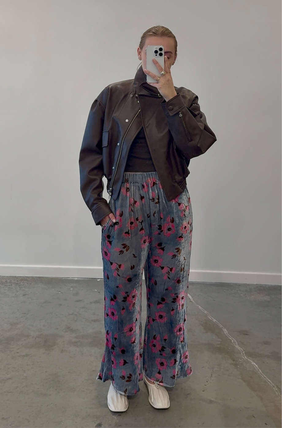Full front view of a woman wearing a brown leather jacket paired with Anntian silver and pink floral velvet wide leg pants at Alas Eius.