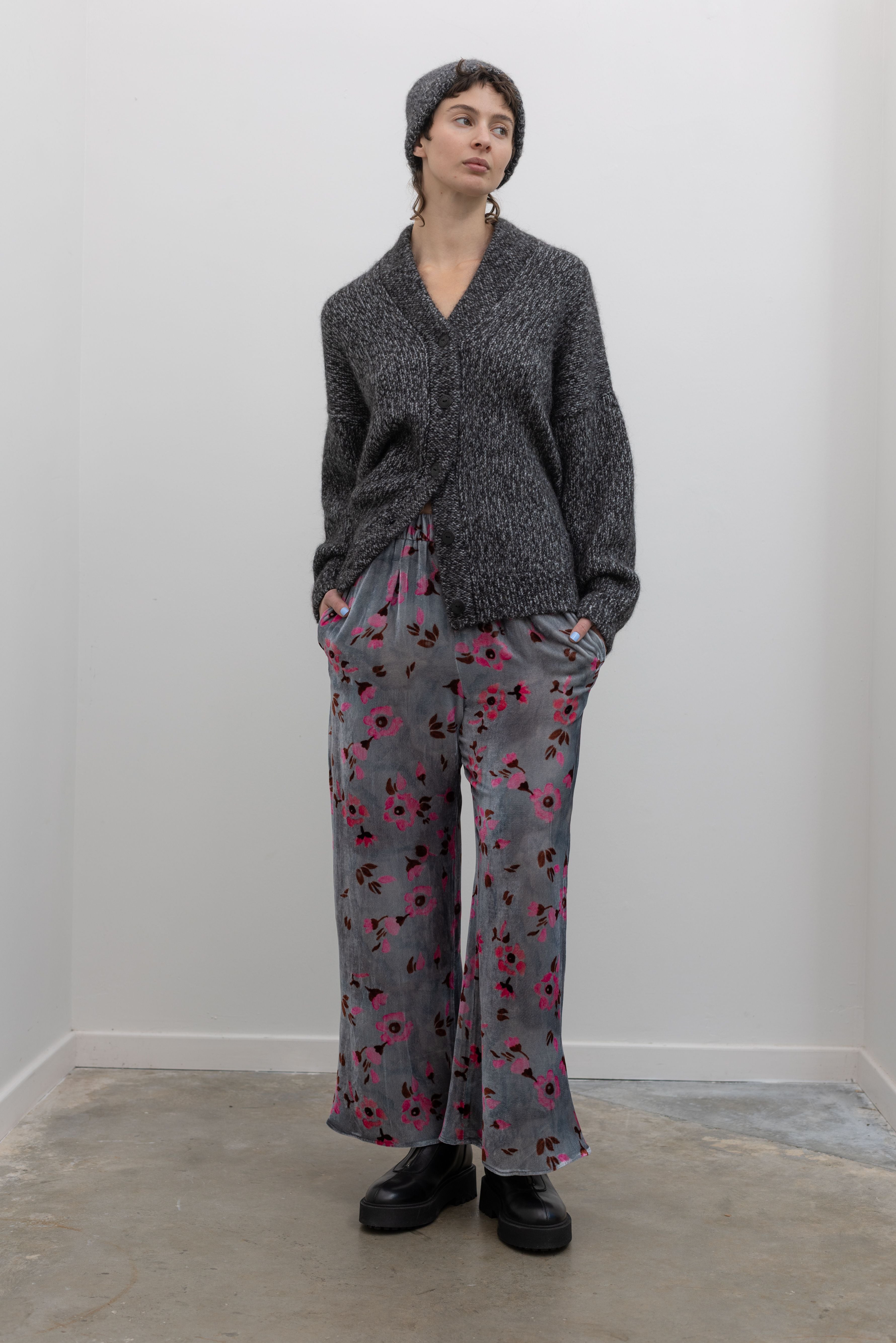 Full front view of a person wearing a dark heathered gray knit cardigan paired with Anntian silver and pink floral velvet wide leg pants at Alas Eius.