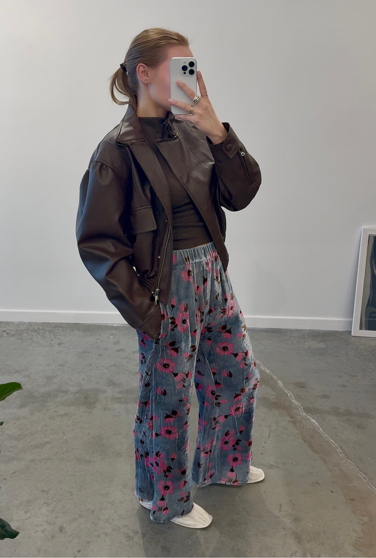 Full side view of a woman wearing a brown leather jacket paired with Anntian silver and pink floral velvet wide leg pants at Alas Eius.