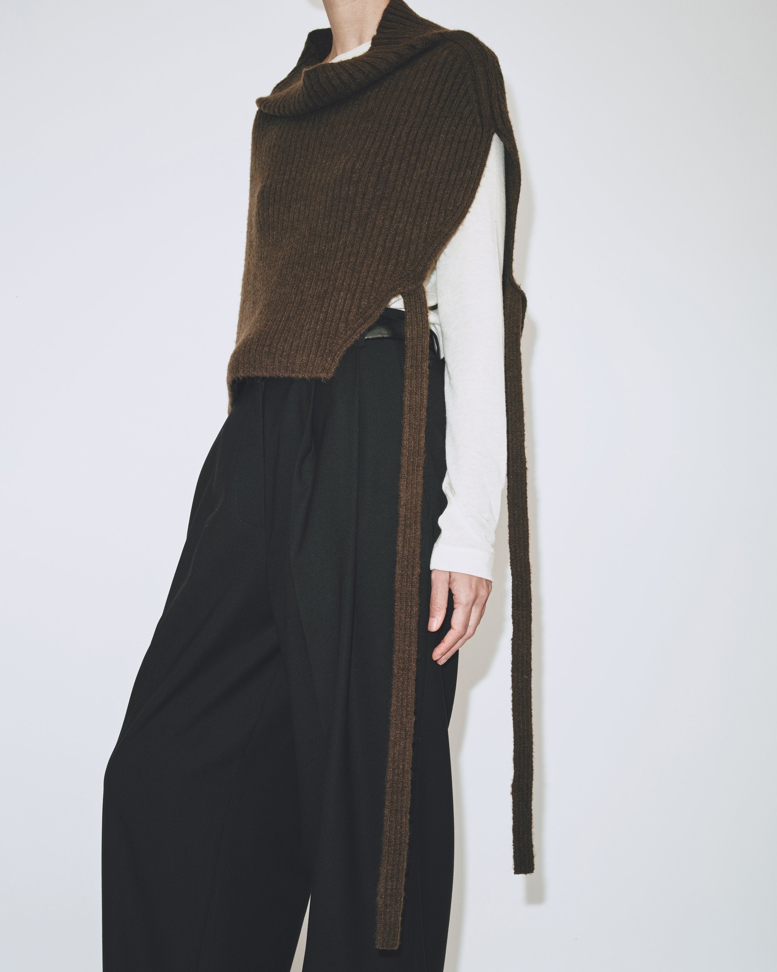 A person wearing an olive brown ribbed knitted Mijeong Park neck warmer with a mock neck neckline and tie waist detail, paired with a black pants at Alas Eius