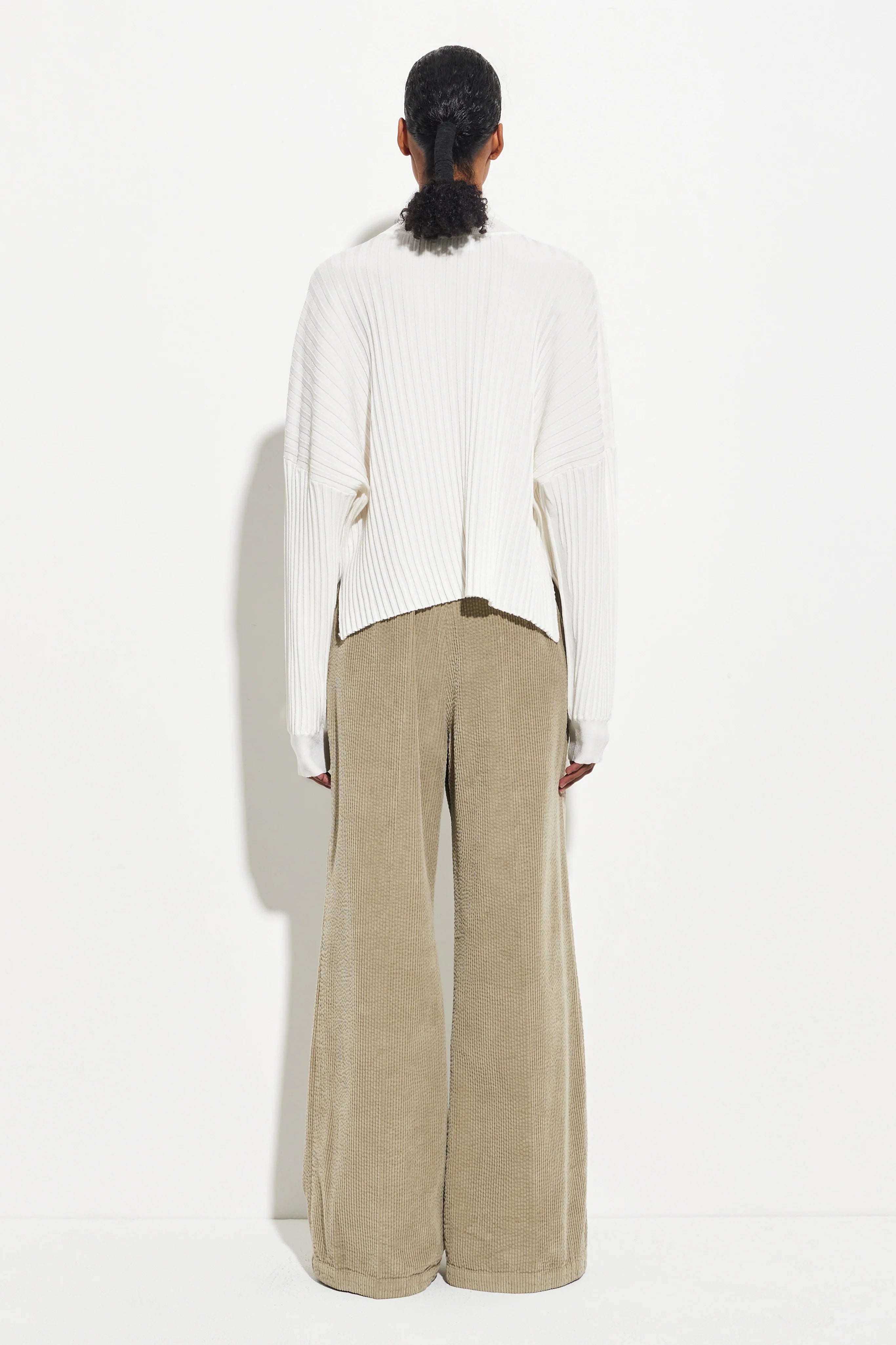Back view of a woman wearing Christian Wijnats Padola Sage Wide Leg Corduroy pants made from garment-dyed cotton and designed with a comfortable elastic waistband, side pockets, and soft front pleats paired with a white long sleeved top  at Alas Eius.