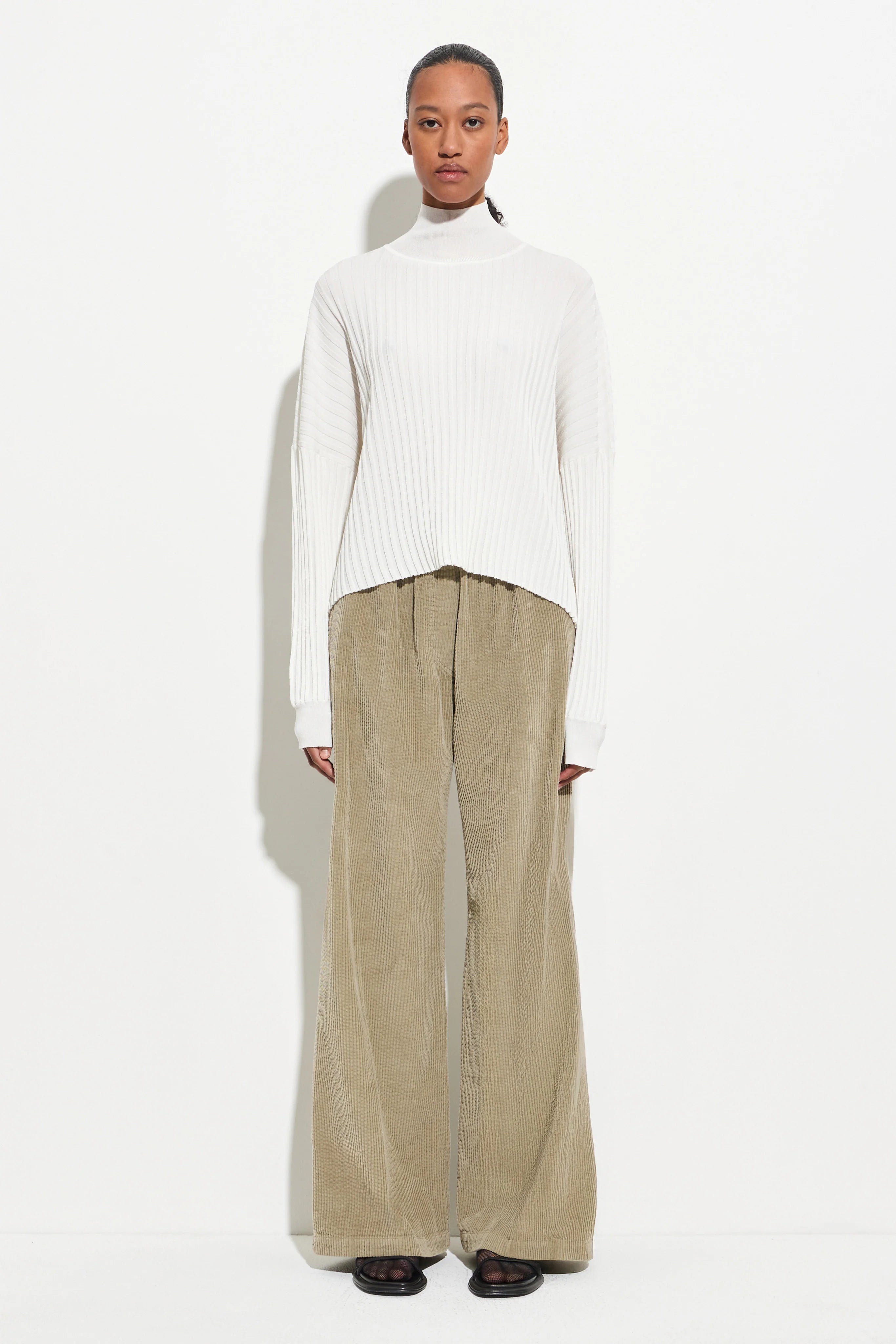 Christian Wijnats Padola Sage Wide Leg Corduroy pants made from garment-dyed cotton and designed with a comfortable elastic waistband, side pockets, and soft front pleats paired with a white long sleeved top at Alas Eius.