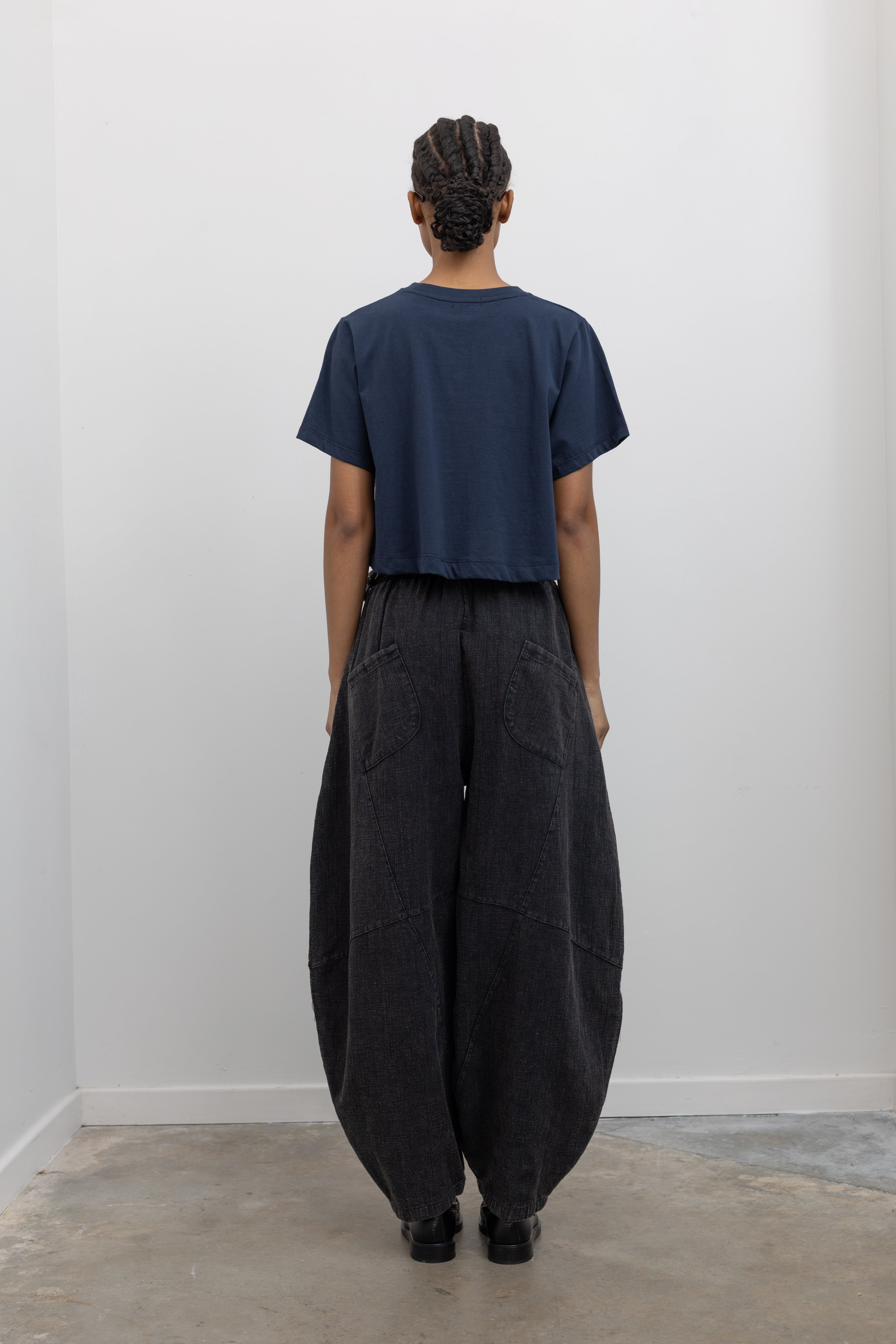 Full length back view of a woman wearing spring contemporary fashion in a Alas Eius label navy blue cropped t-shirt paired with Collective Spring Black Barrel Cotton Blend Pants at Alas Eius. 