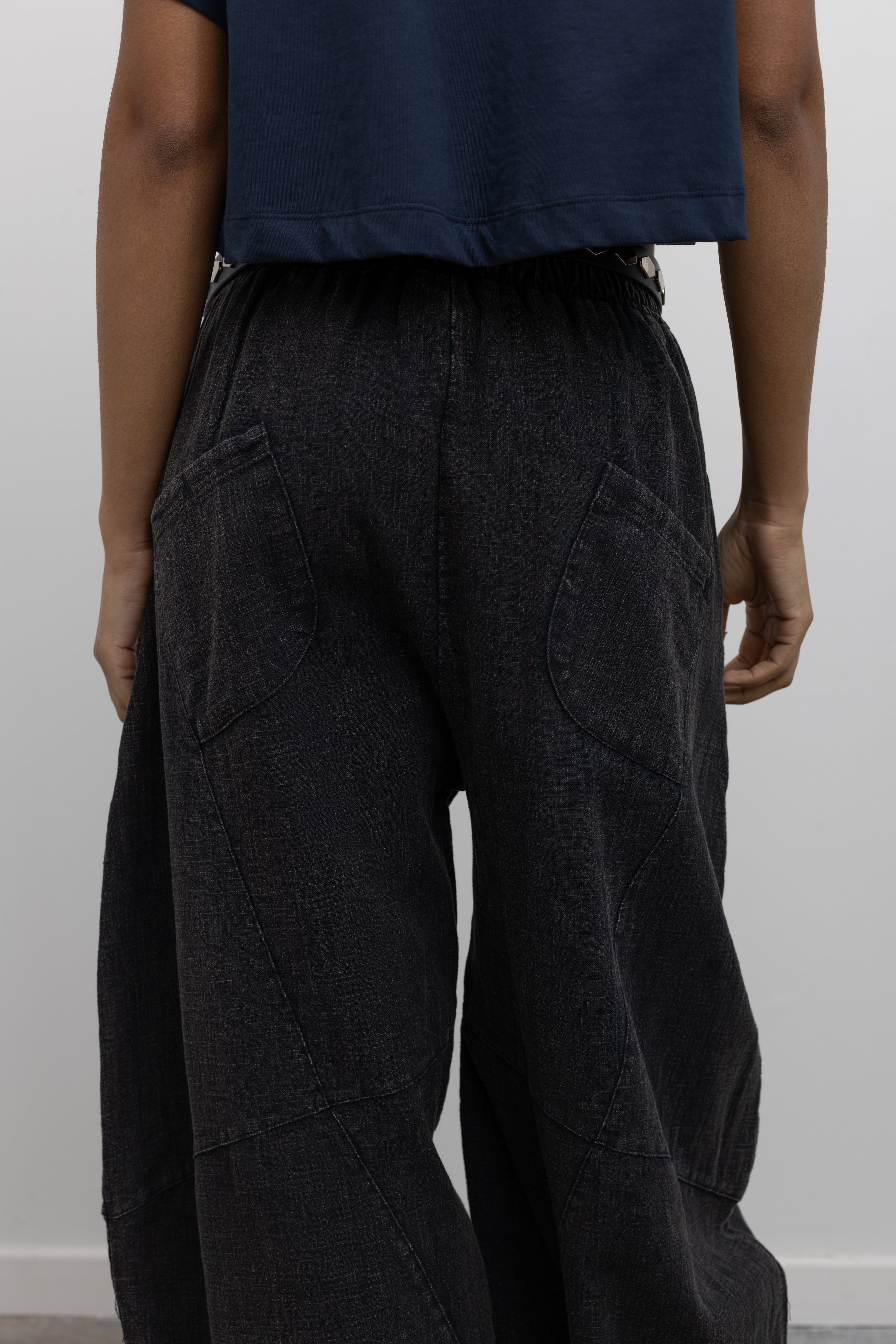 Close-up back view of a woman wearing a spring casual outfit in a Alas Eius label navy blue cropped t-shirt paired with Collective Spring Black Barrel Cotton Blend Pants at Alas Eius. 
