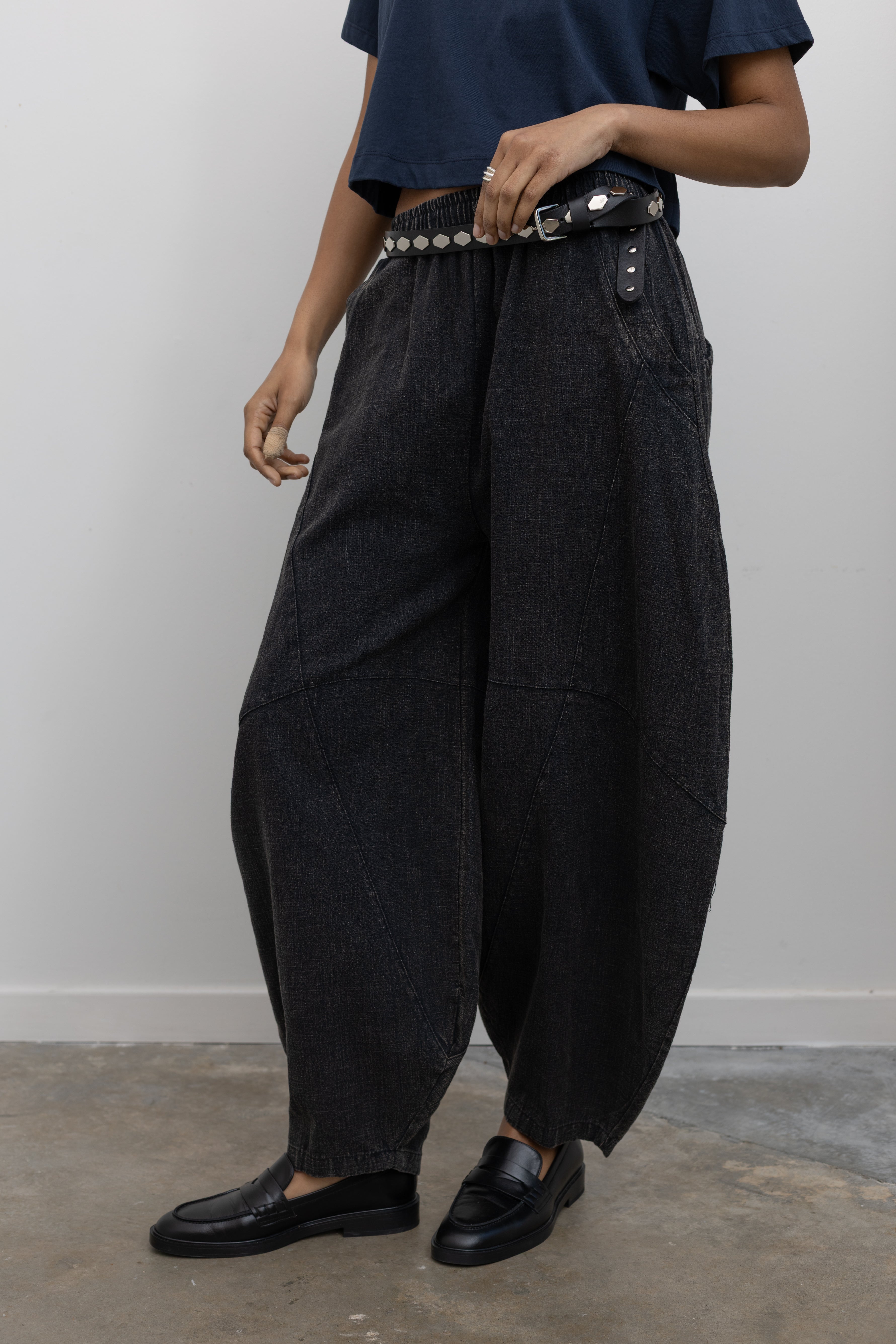 A Woman wearing spring contemporary fashion in a Alas Eius label navy blue cropped t-shirt paired with Collective Spring Black Barrel Cotton Blend Pants with black leather loafers at Alas Eius. 