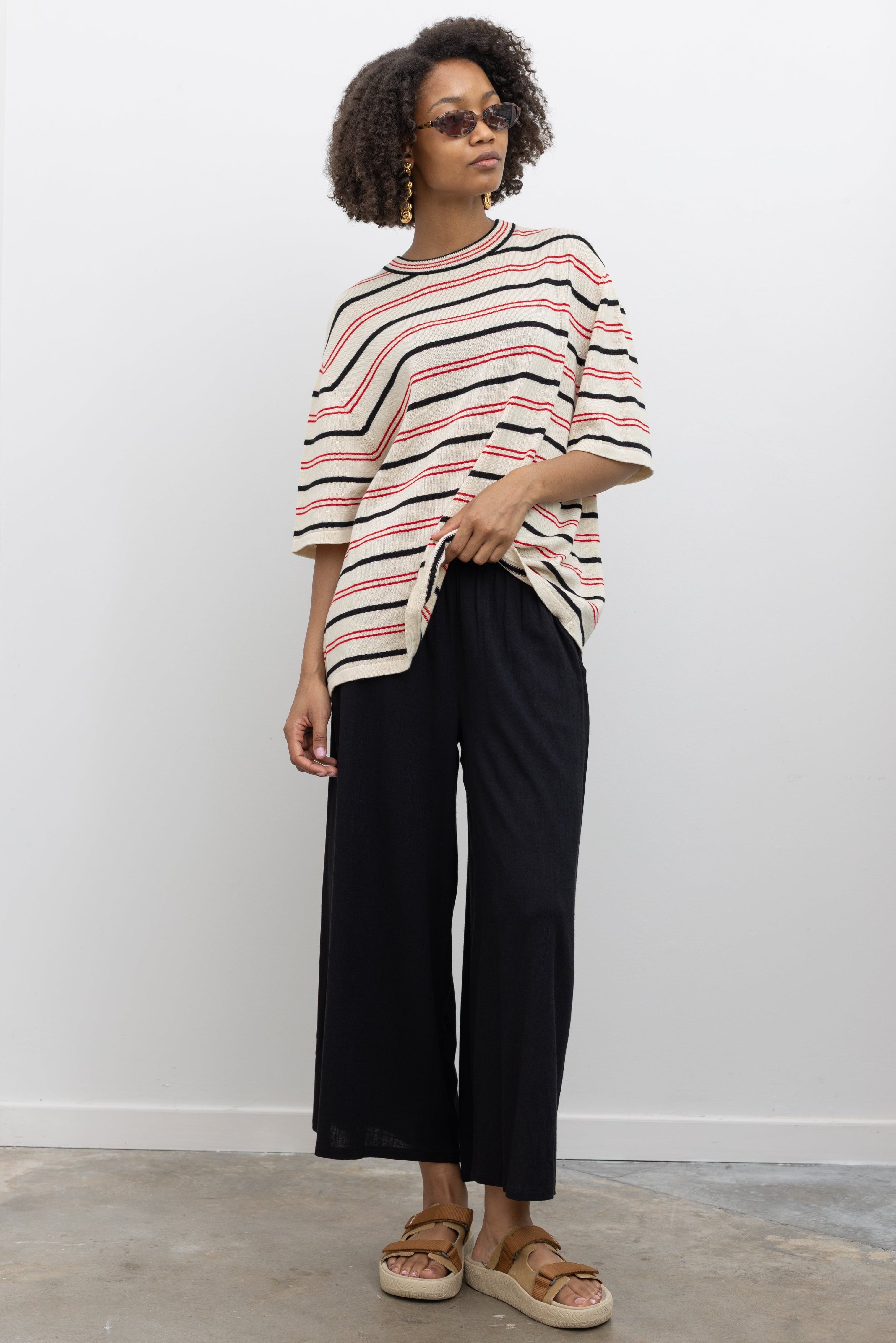 Woman wearing chic summer fashion in Collective black elastic waistband flowy pull on cropped pants with a Cordera organic cotton striped t-shirt and Veja tan suede slide sandals at Alas Eius. 