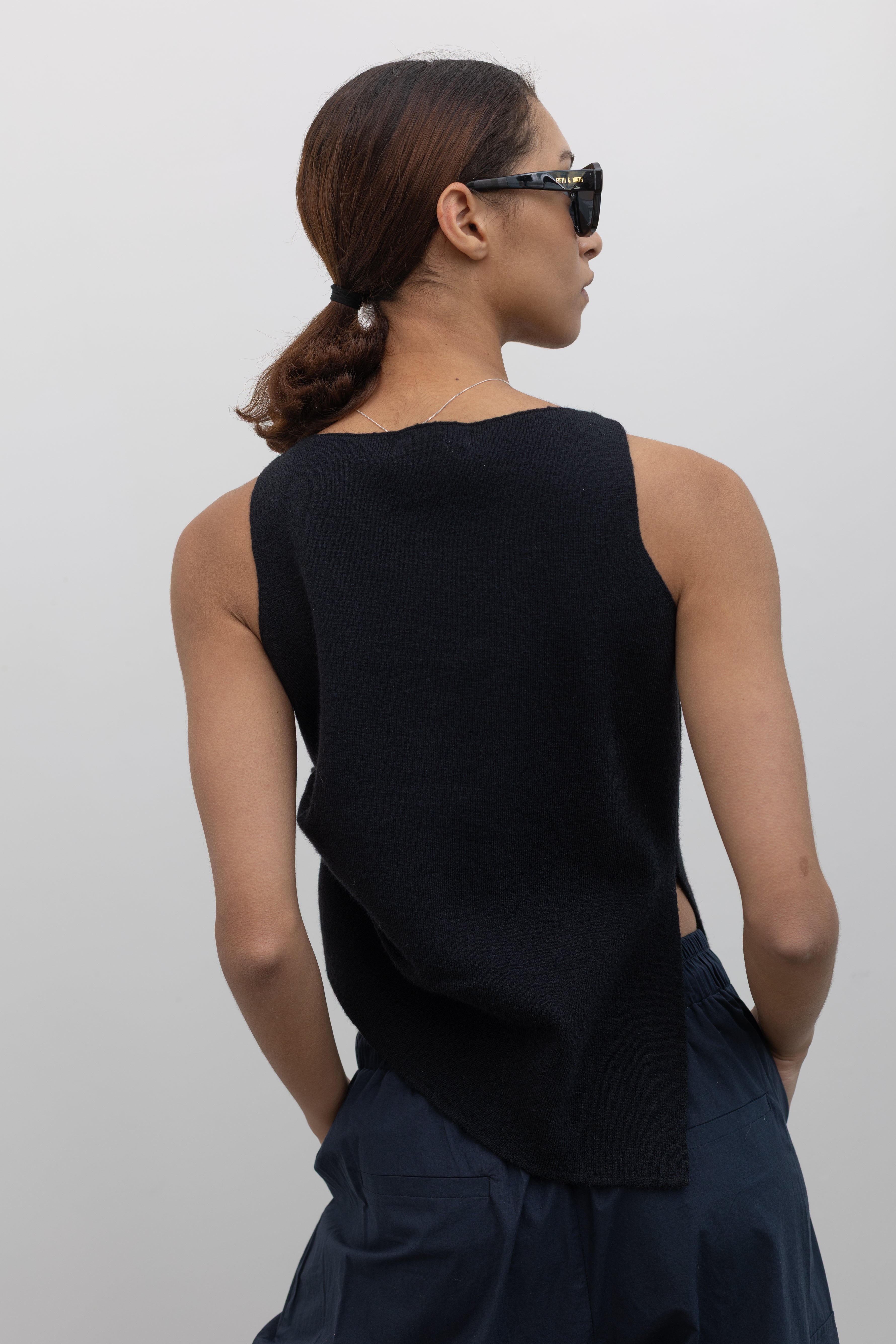 Close-up back view of a woman wearing a modern and sophisticated Collective Black shirring knit top featuring an asymmetrical hem, paired with an Alas Eius navy blue cargo pant.