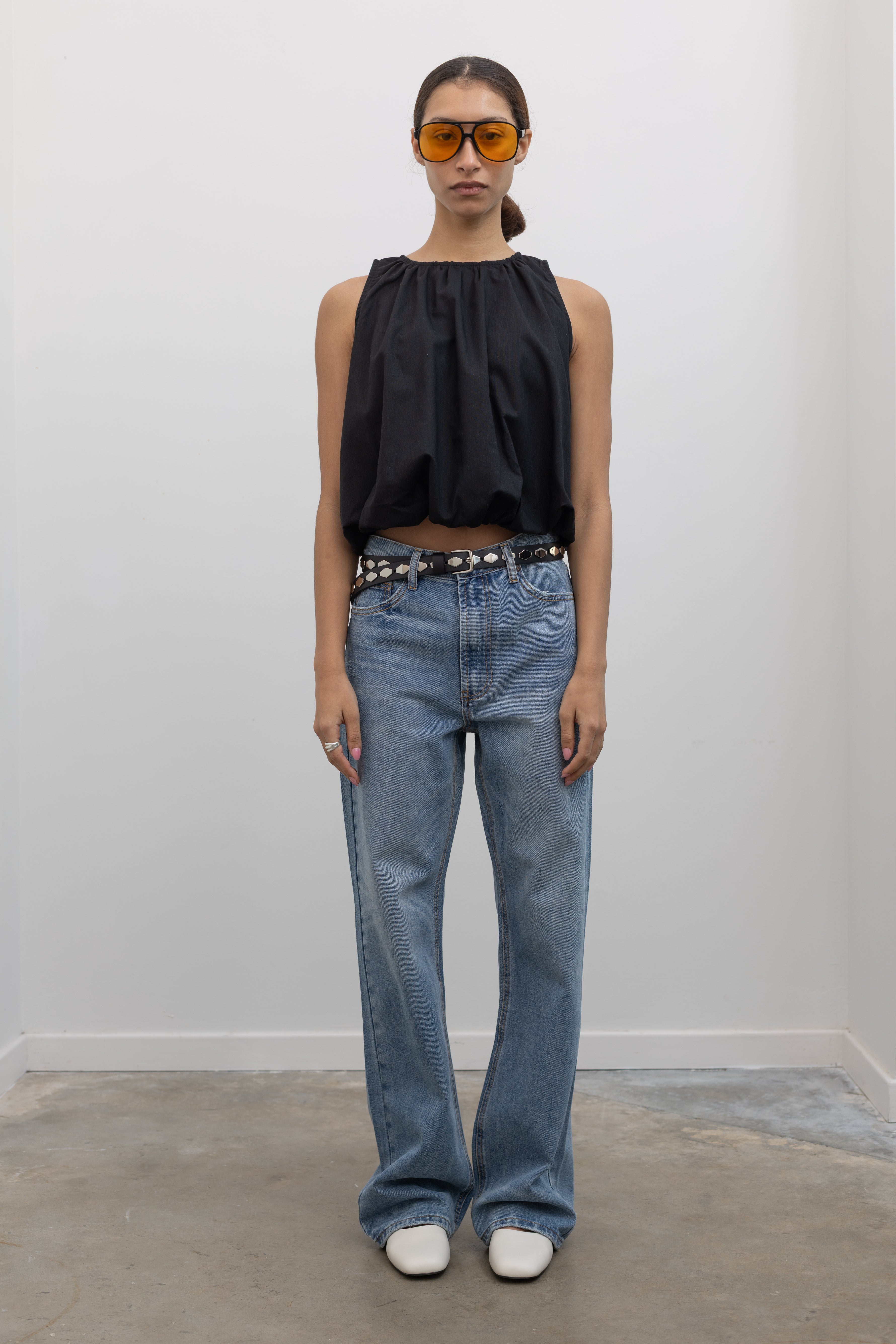 Full length view of a woman wearing an elevated classic essential accessory in a Collective brand Italian black leather belt with shiny silver honeycomb shaped hardware paired with light wash denim jeans and a black balloon hem top at Alas Eius. 