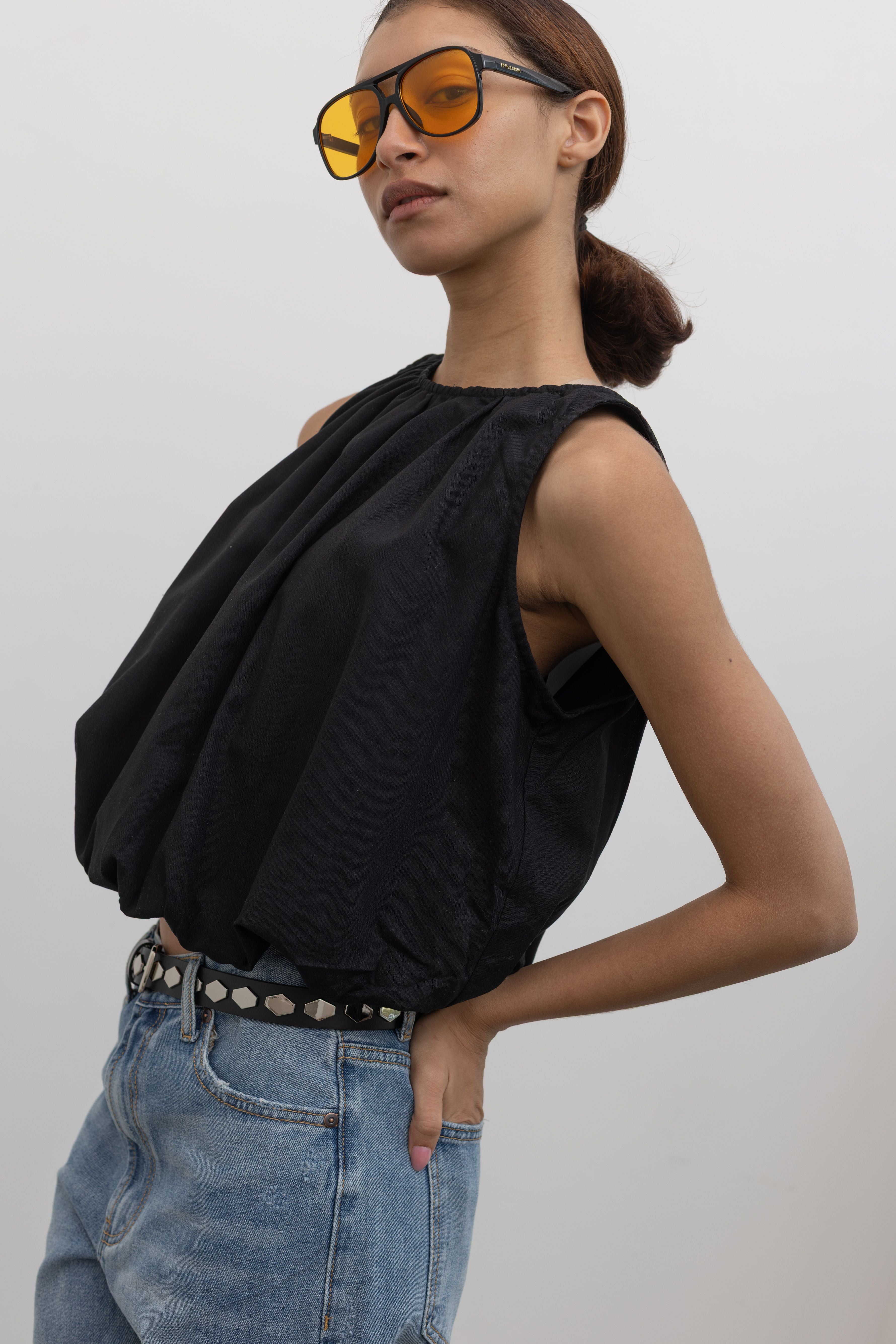 Woman posing wearing Spring fashion in a Collective black linen bubble hem sleeveless top paired with light wash denim jeans and a silver hardware studded black leather belt at Alas Eius.