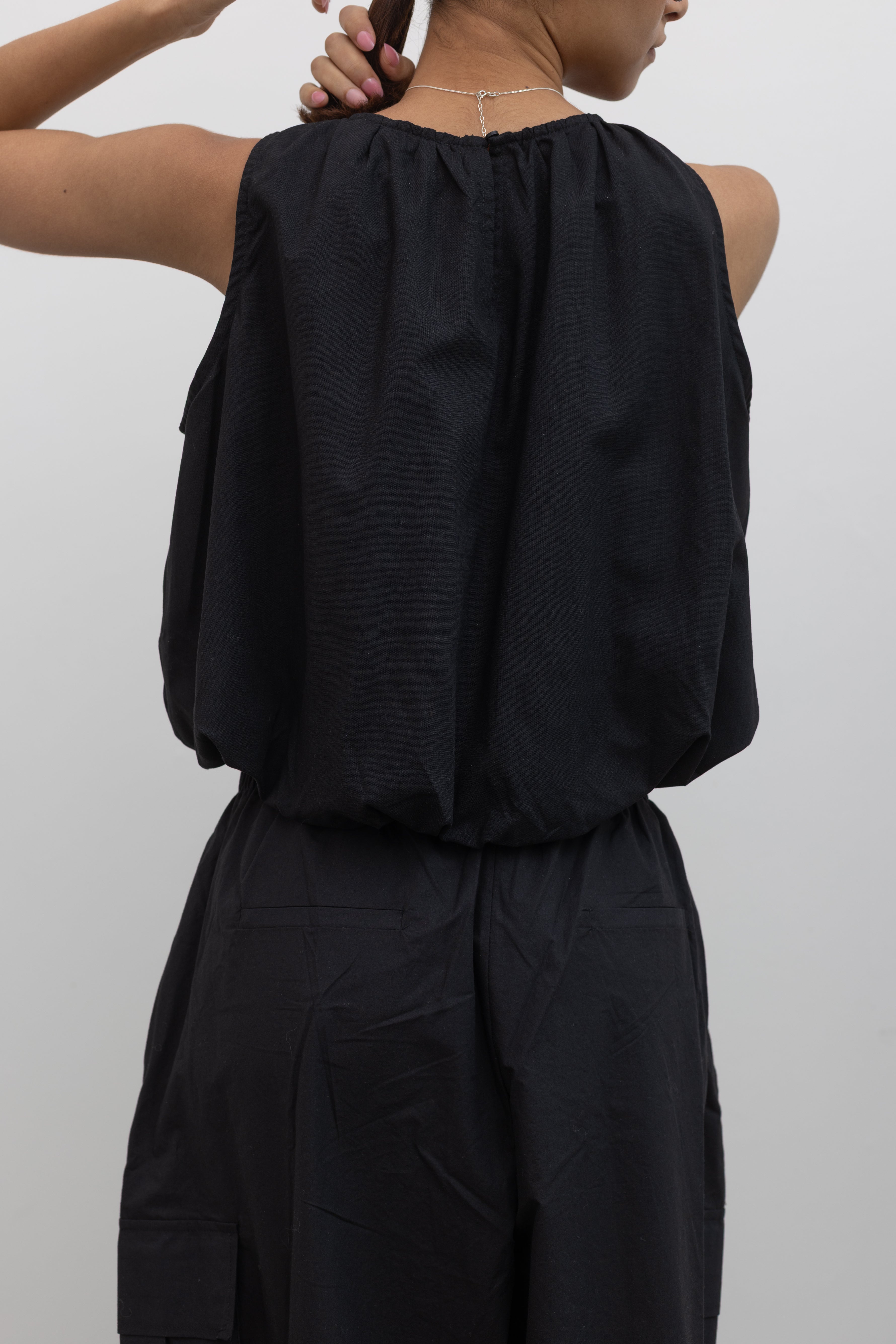 Back view of a woman posing wearing Spring fashion in a Collective black linen bubble hem sleeveless top at Alas Eius.