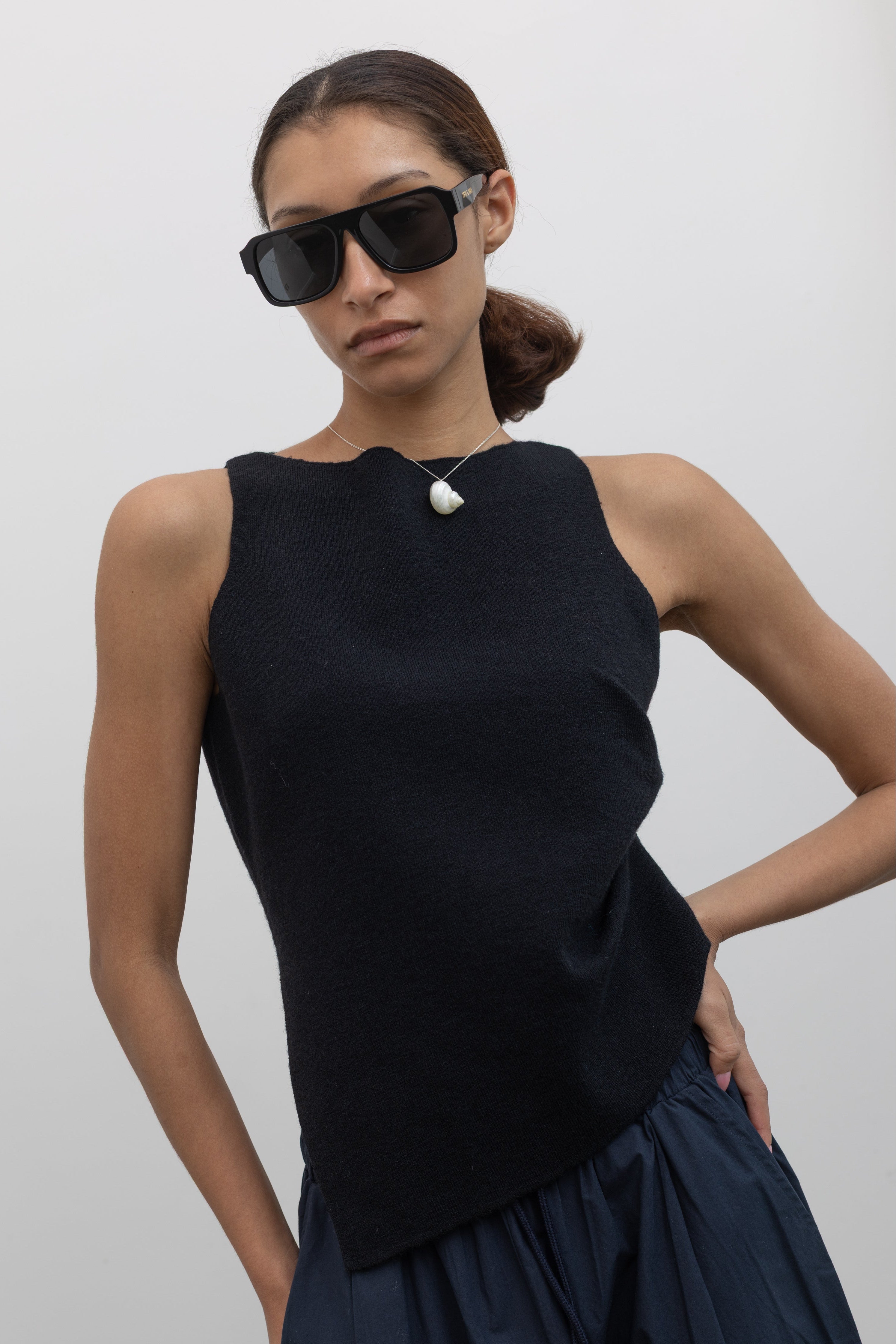 Close-up front view of a woman wearing a modern and sophisticated Collective Black shirring knit top featuring an asymmetrical hem, paired with an Alas Eius navy blue cargo pant.