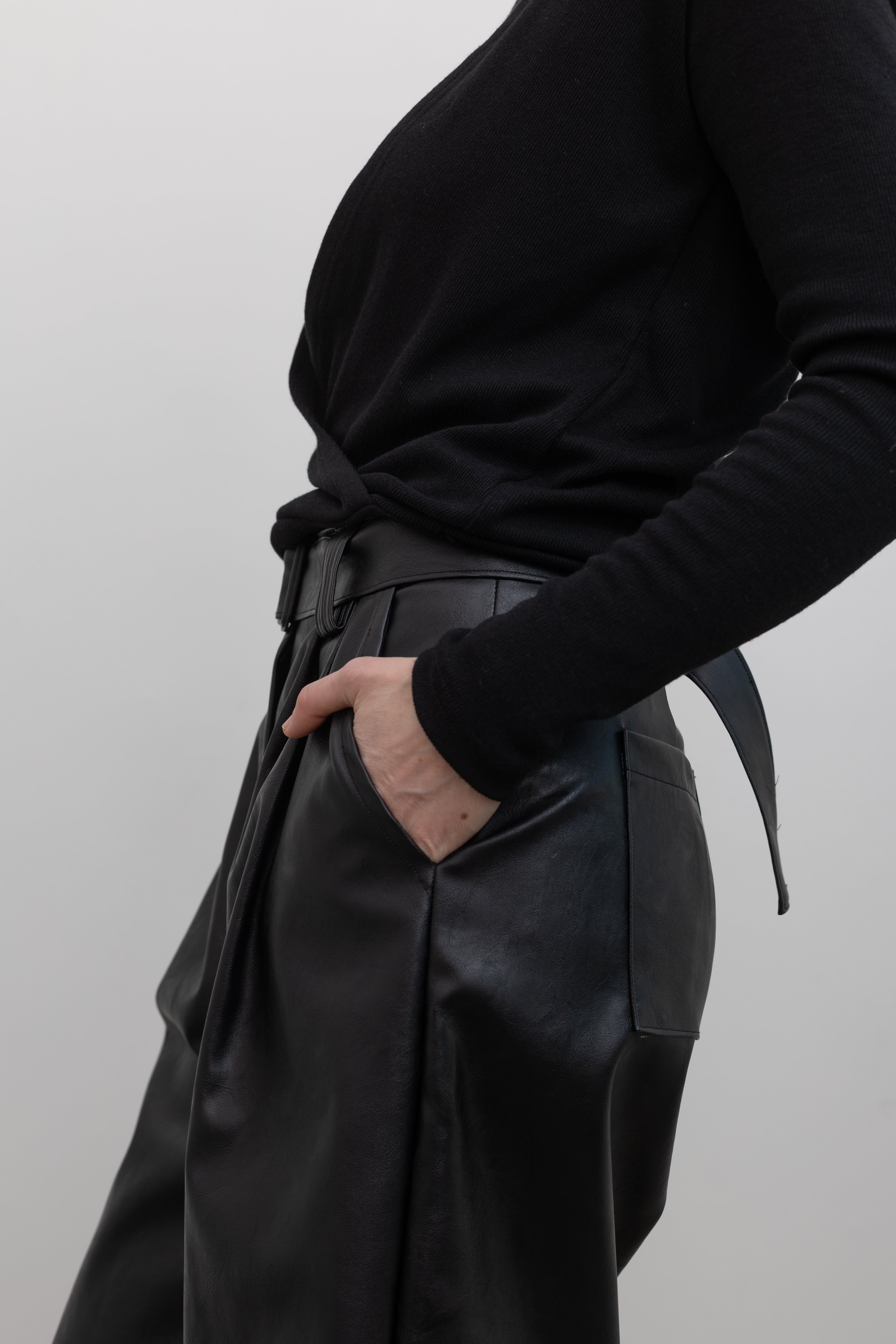 Close-up side view of a woman wearing Collective label Black Vegan Leather Belted Bermuda Shorts with an Alas Eius label mock neck sweater at Alas Eius.