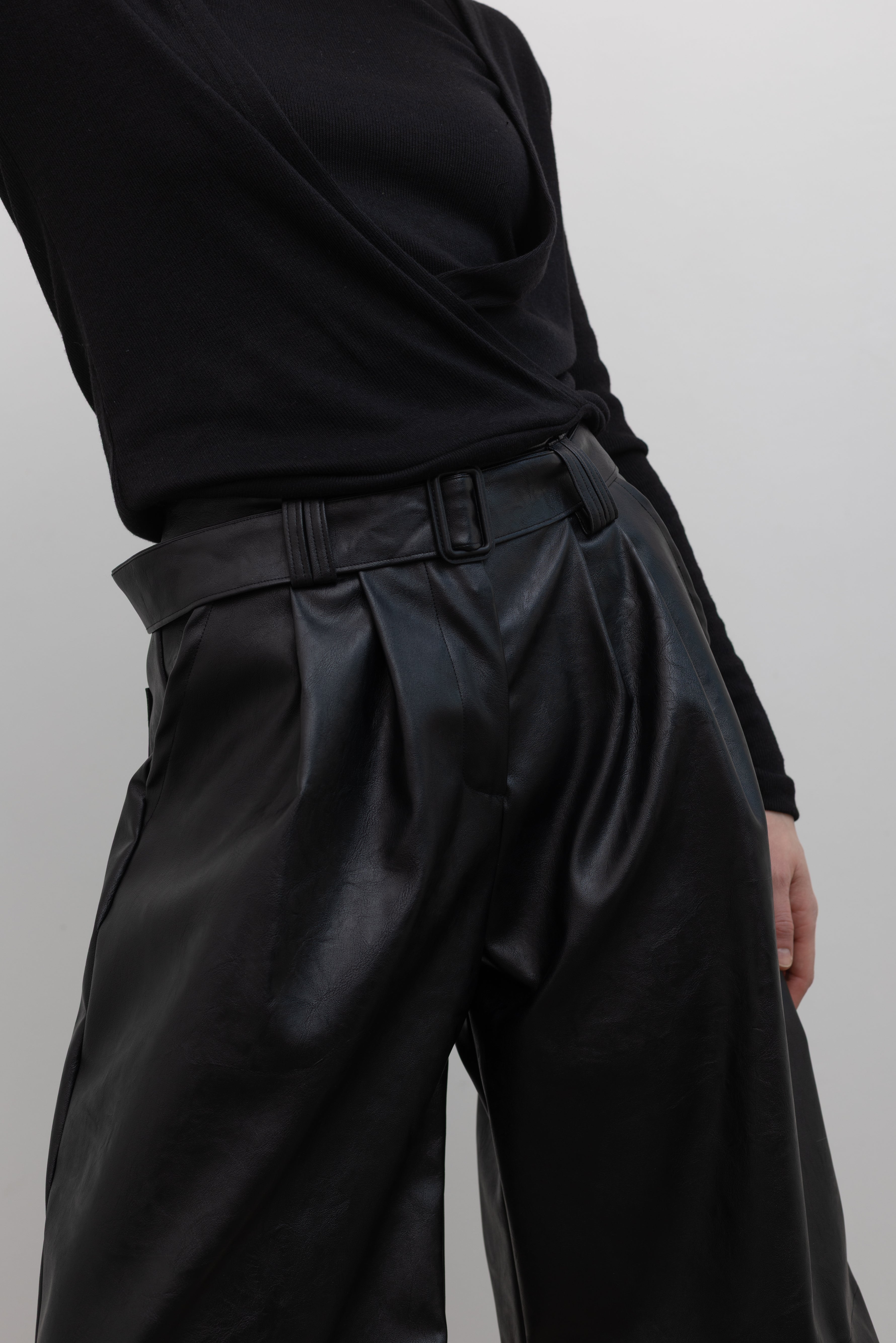 Close-up front view of a woman wearing Collective label Black Vegan Leather Belted Bermuda Shorts at Alas Eius.