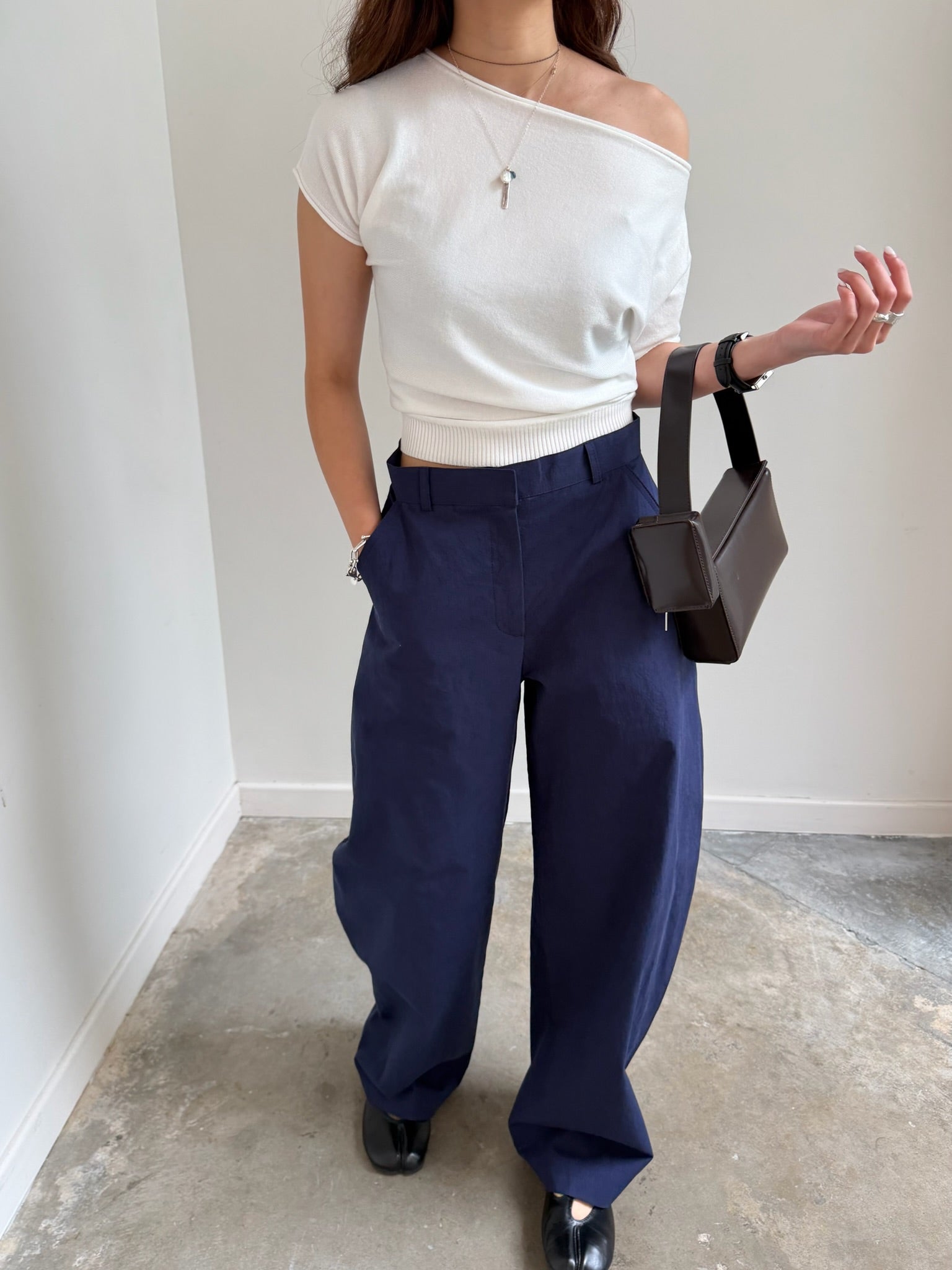 Woman wearing modern minimalist fashion in the Collective blue cotton barrel leg trouser with a white asymmetrical top, black tabi flats, and a St. Agni leather bag at Alas Eius. 