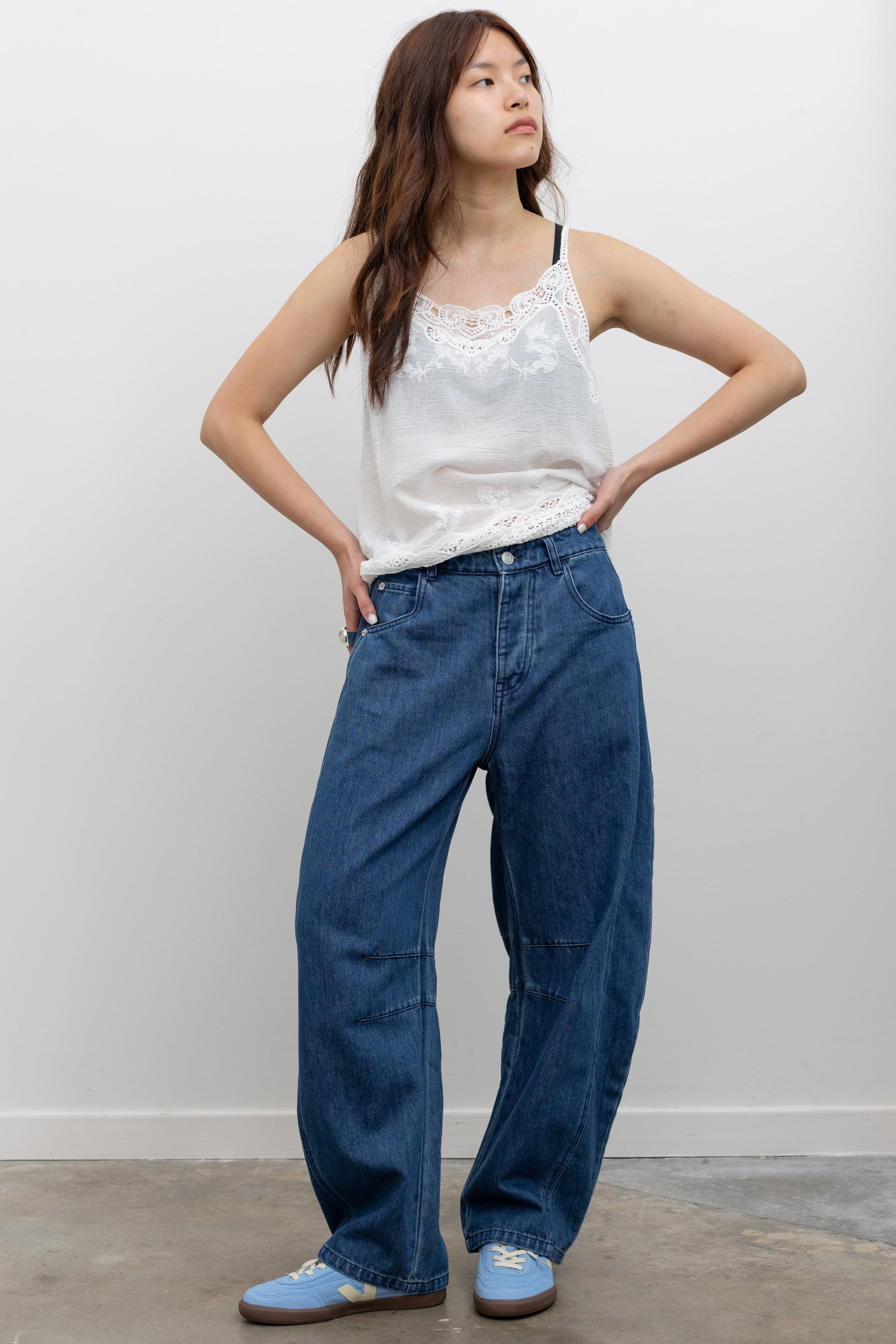 Collective blue cotton baggy denim pants with curved balloon silhouette, mid-rise waist, and full-length hem paired with a crochet lace camisole tank top and Veja blue suede sneakers at Alas Eius. 