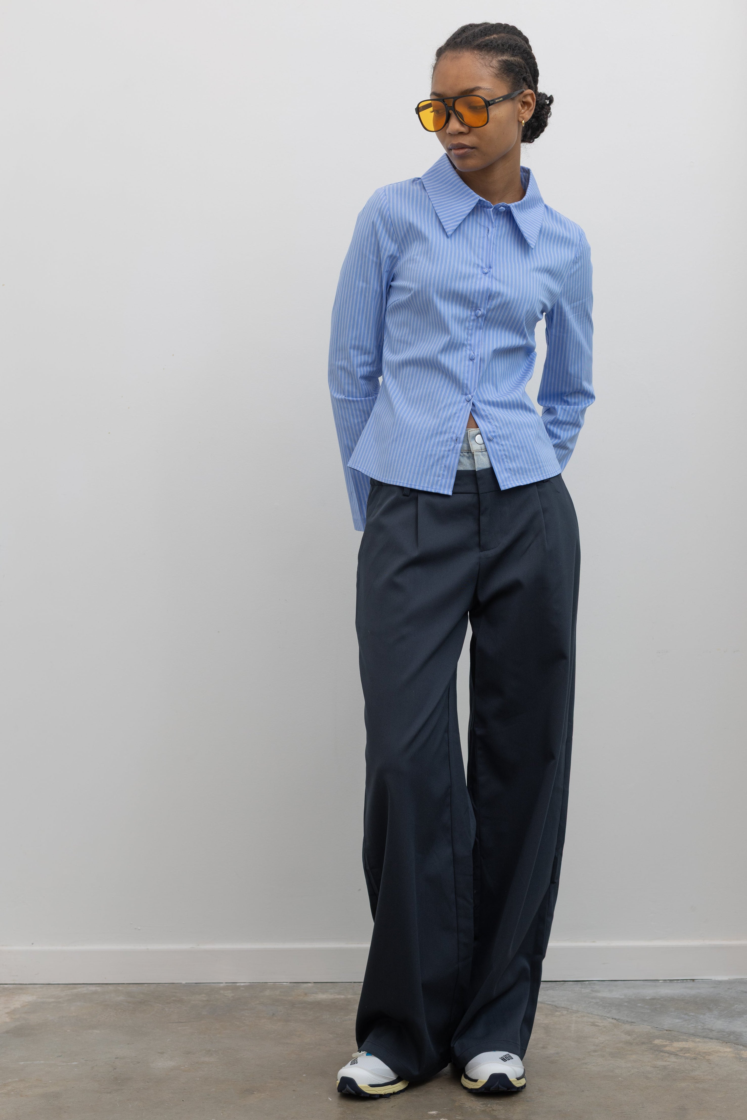 Front view of a woman standing wearing Spring fashion in a Collective Blue Pinstripe Tailored Slim-Fit Button Down Top paired with blue wide leg pants and sneakers at Alas Eius.