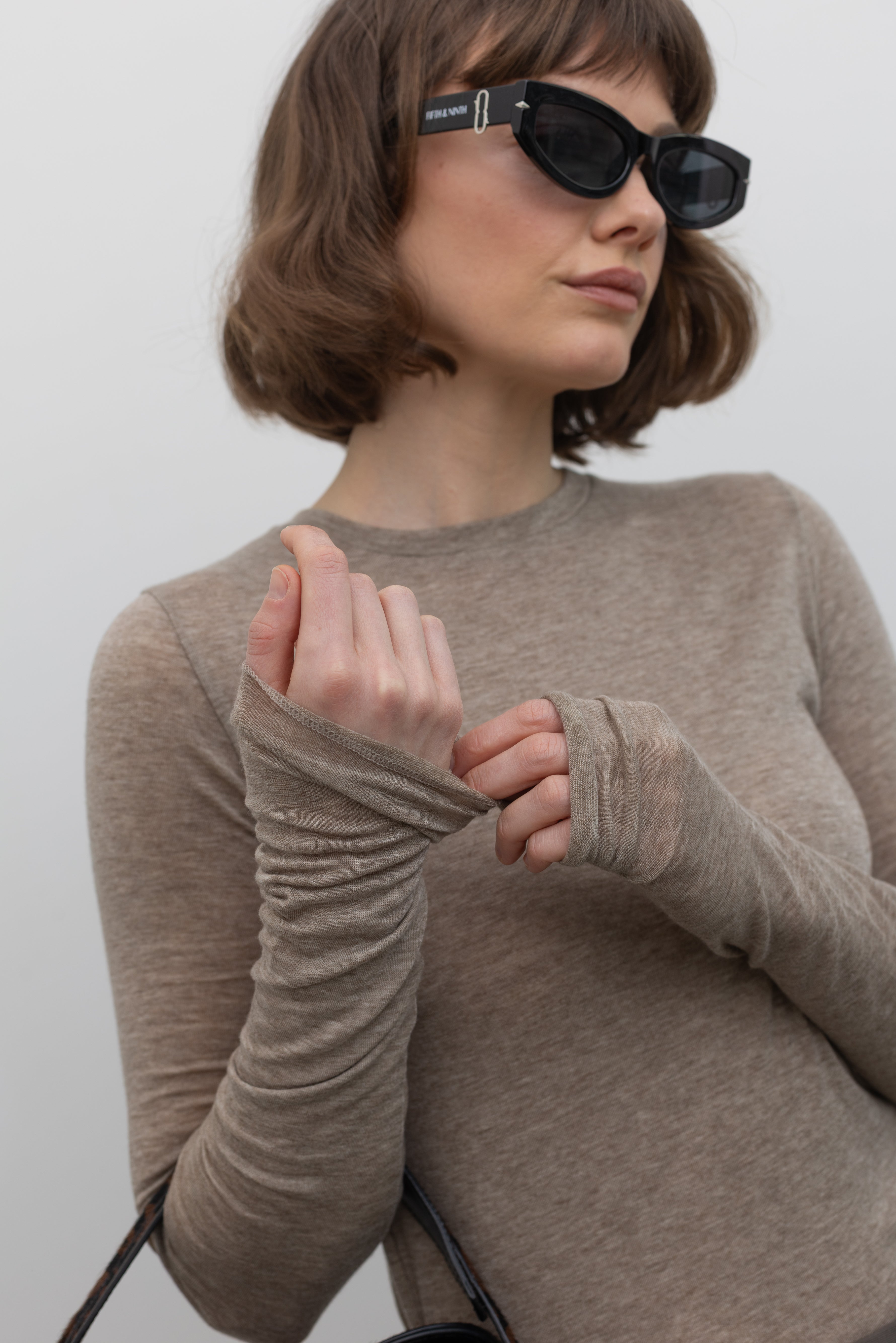 Close-up front view of a woman wearing an elevated capsule wardrobe essential in a Collective Brand Beige Merino Wool Long Sleeve Fitted Top at Alas Eius. 