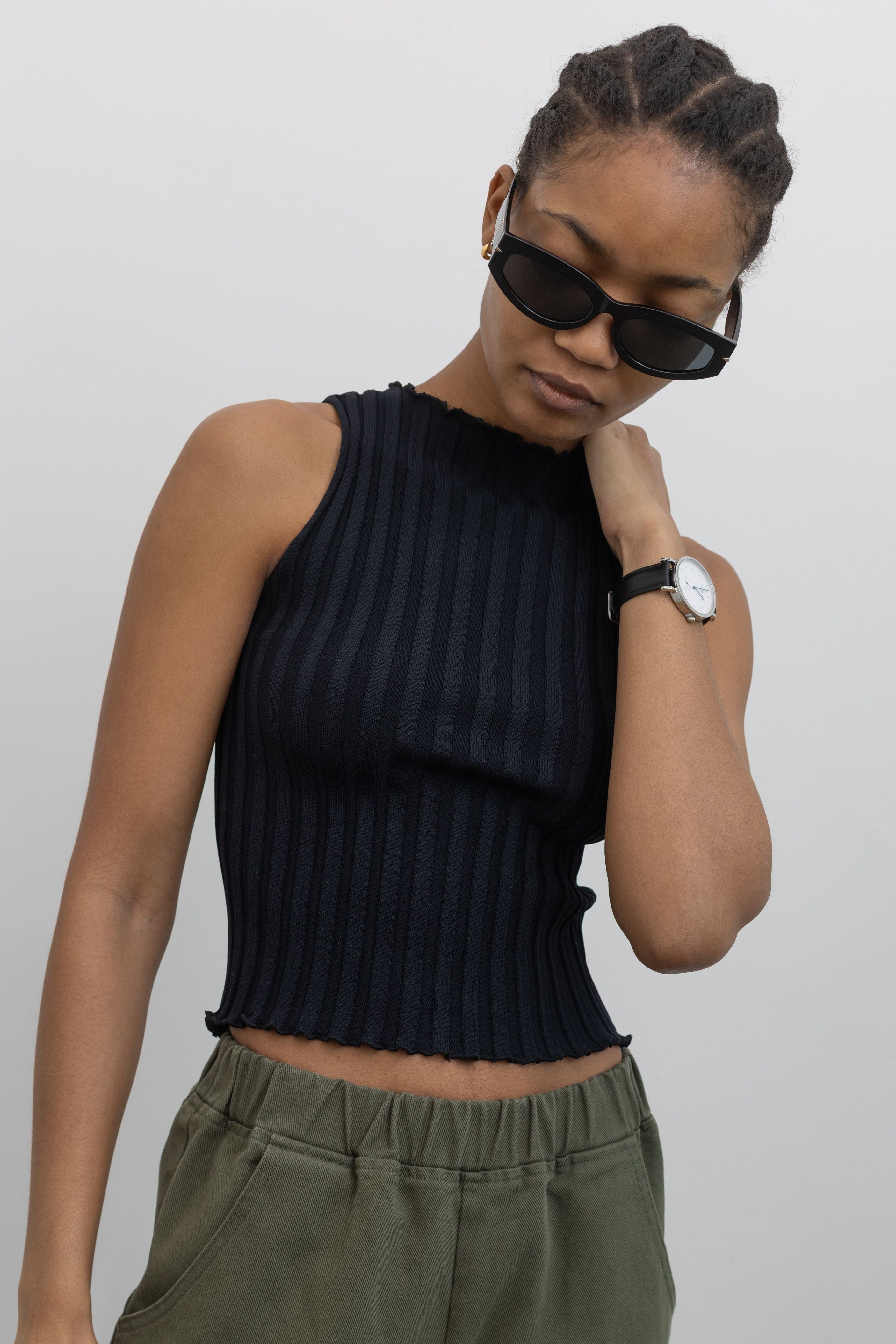 Close-up front view of a woman wearing spring capsule wardrobe essential in a Collective brand black fitted ribbed knit lettuce hem sleeveless top with slight mock neck paired with Le Bon Shoppe olive green cotton canvas arc shaped pant at Alas Eius. 