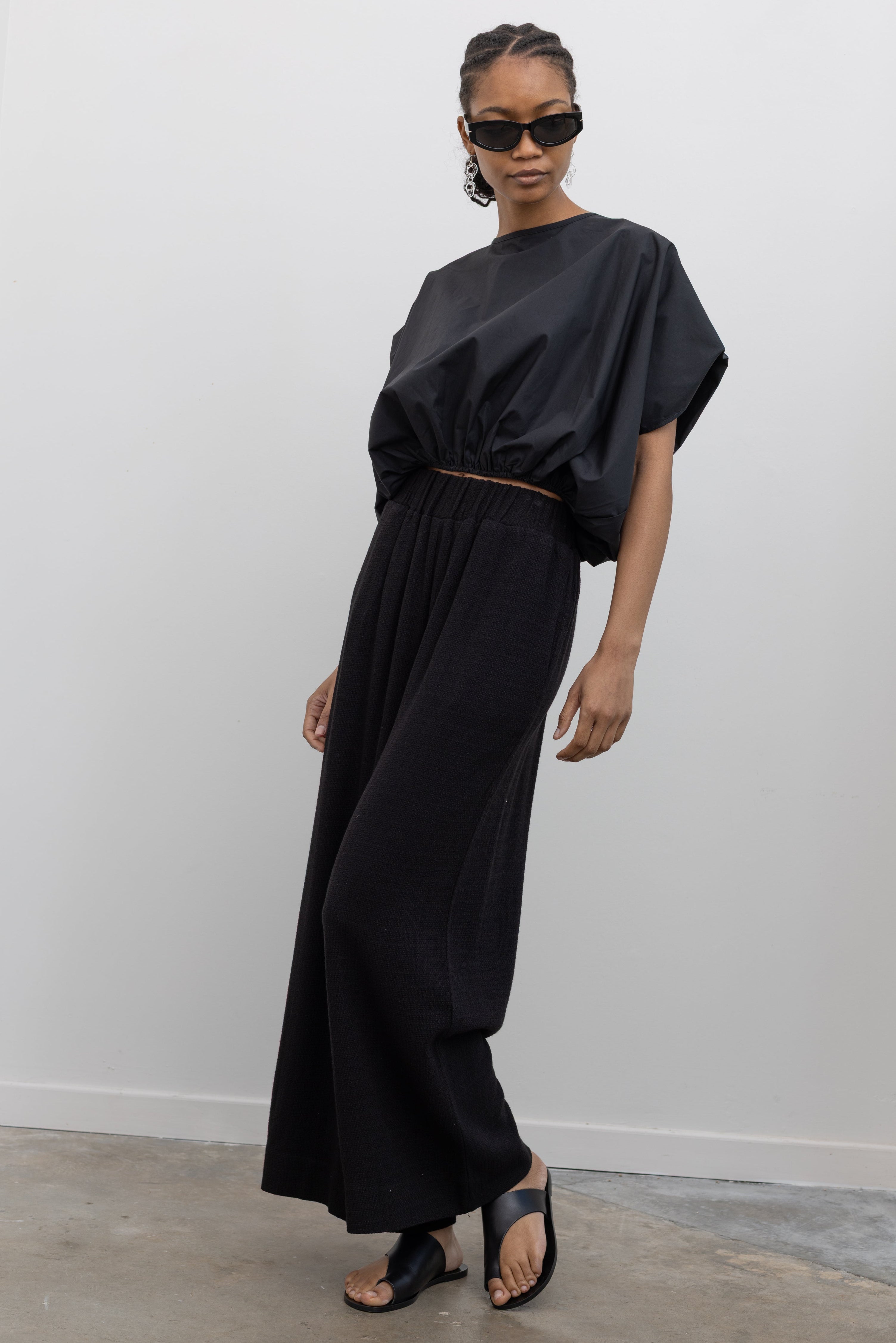 Full length view of a woman posing wearing chic and sophisticated spring fashion in the Collective brand black linen wide leg pull on pants with a black balloon hem top and ATP black leather cutout sandals at an Alas Eius store. 