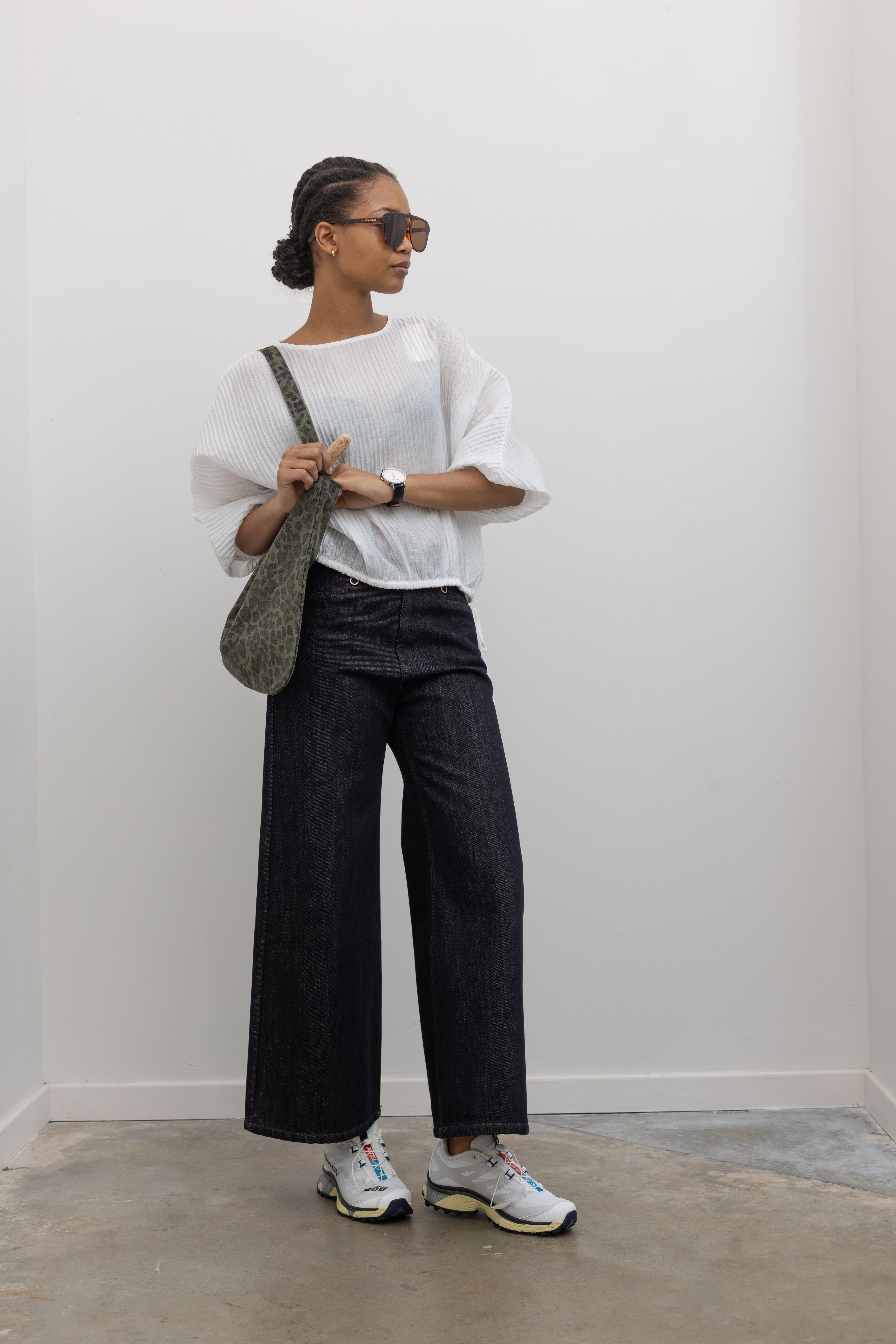 Full length view of a woman wearing Collective brand dark wash fleece lined wide-leg, high-rise jeans with squared off pockets with silver hardware paired with Salomon sneakers at Alas Eius.