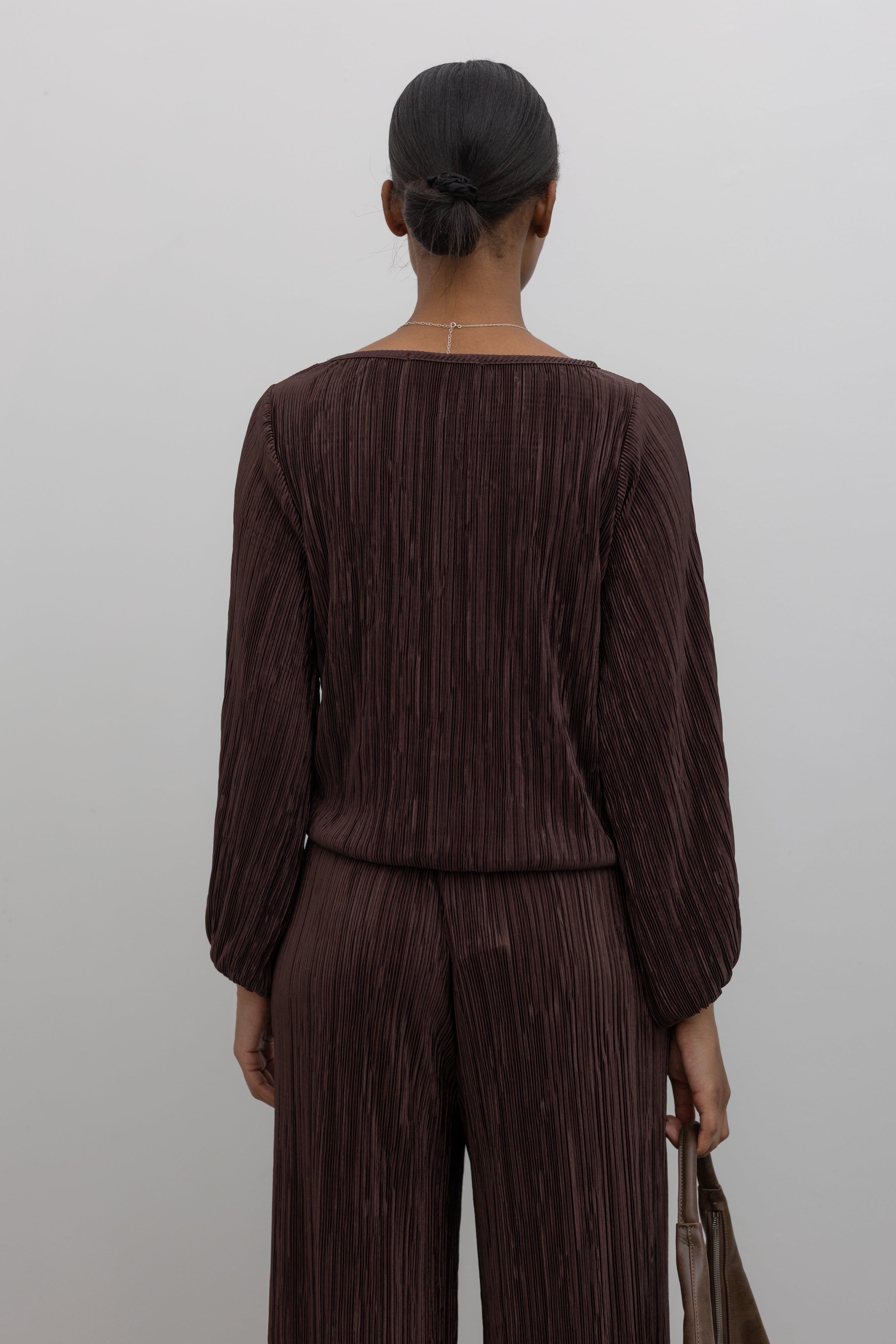 Back view of a woman wearing a flattering chocolate brown plisse long sleeve top with its coordinating pants creating the perfect elevated or casual outfit. 