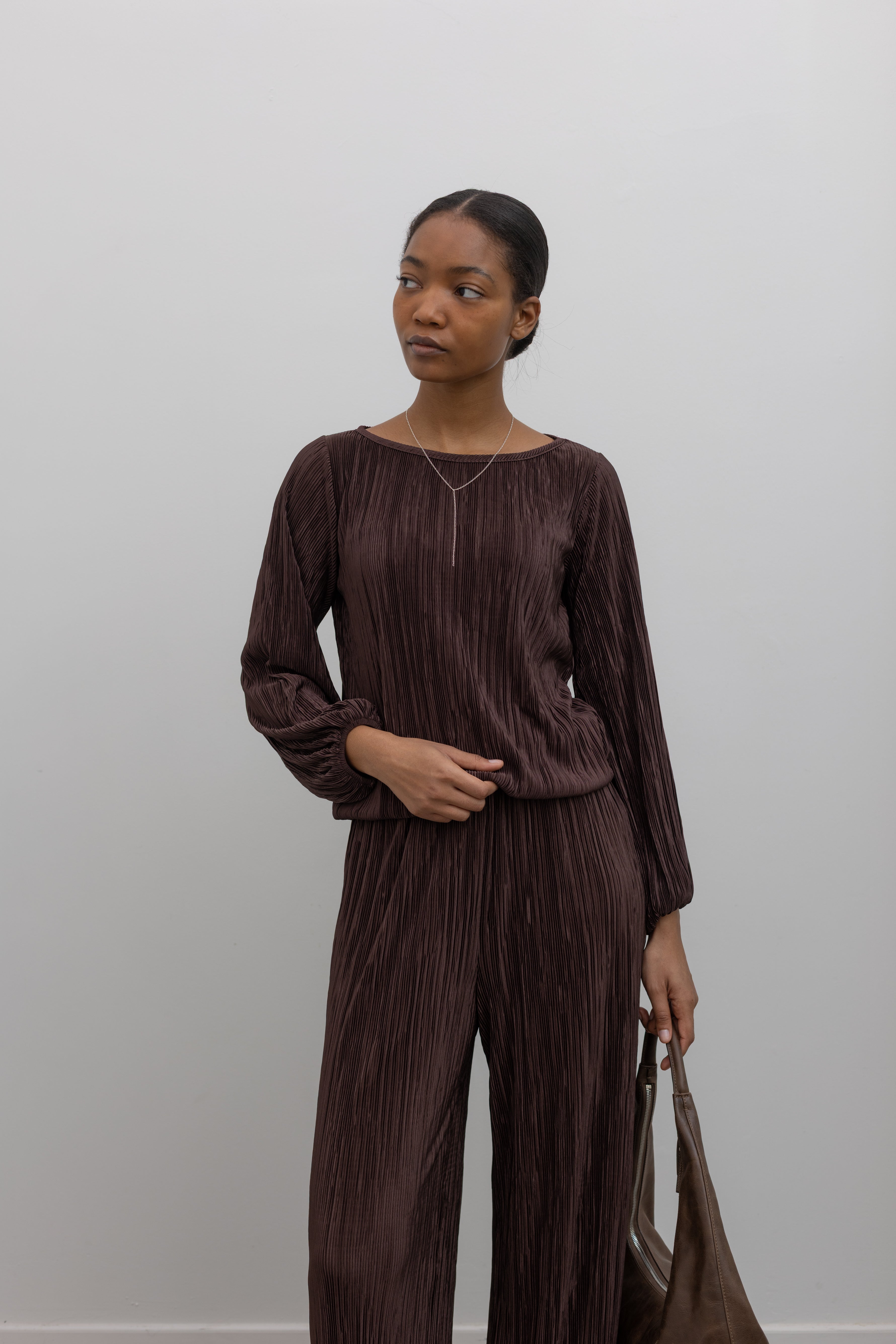 Woman posing wearing a modest chocolate brown plisse long sleeve top with its coordinating pants creating the perfect elevated or casual outfit. 