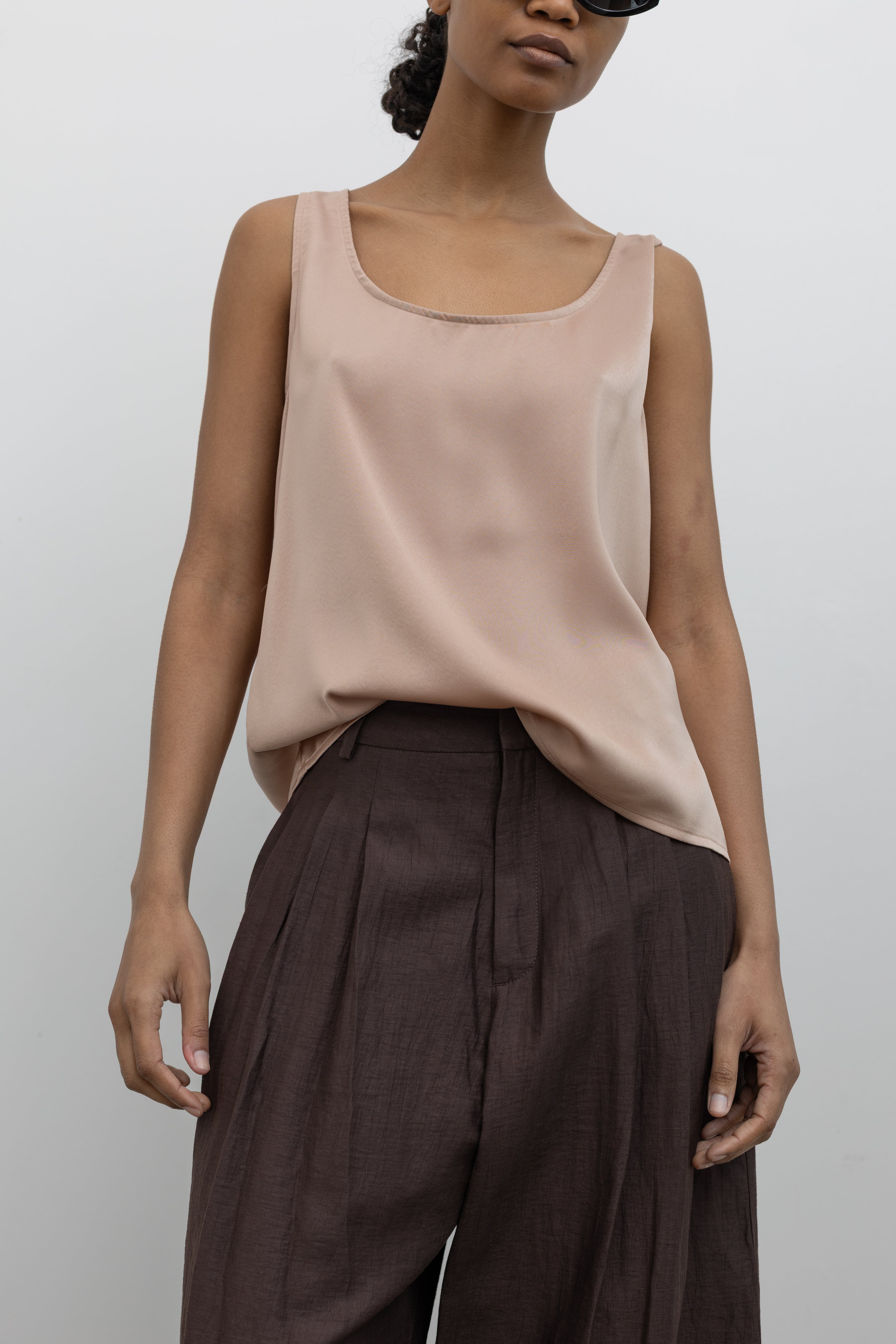 Woman wearing spring workwear essential layering top in a Collective brand solid beige satin tank top with a relaxed flowy fit paired with pleated trouser at Alas Eius