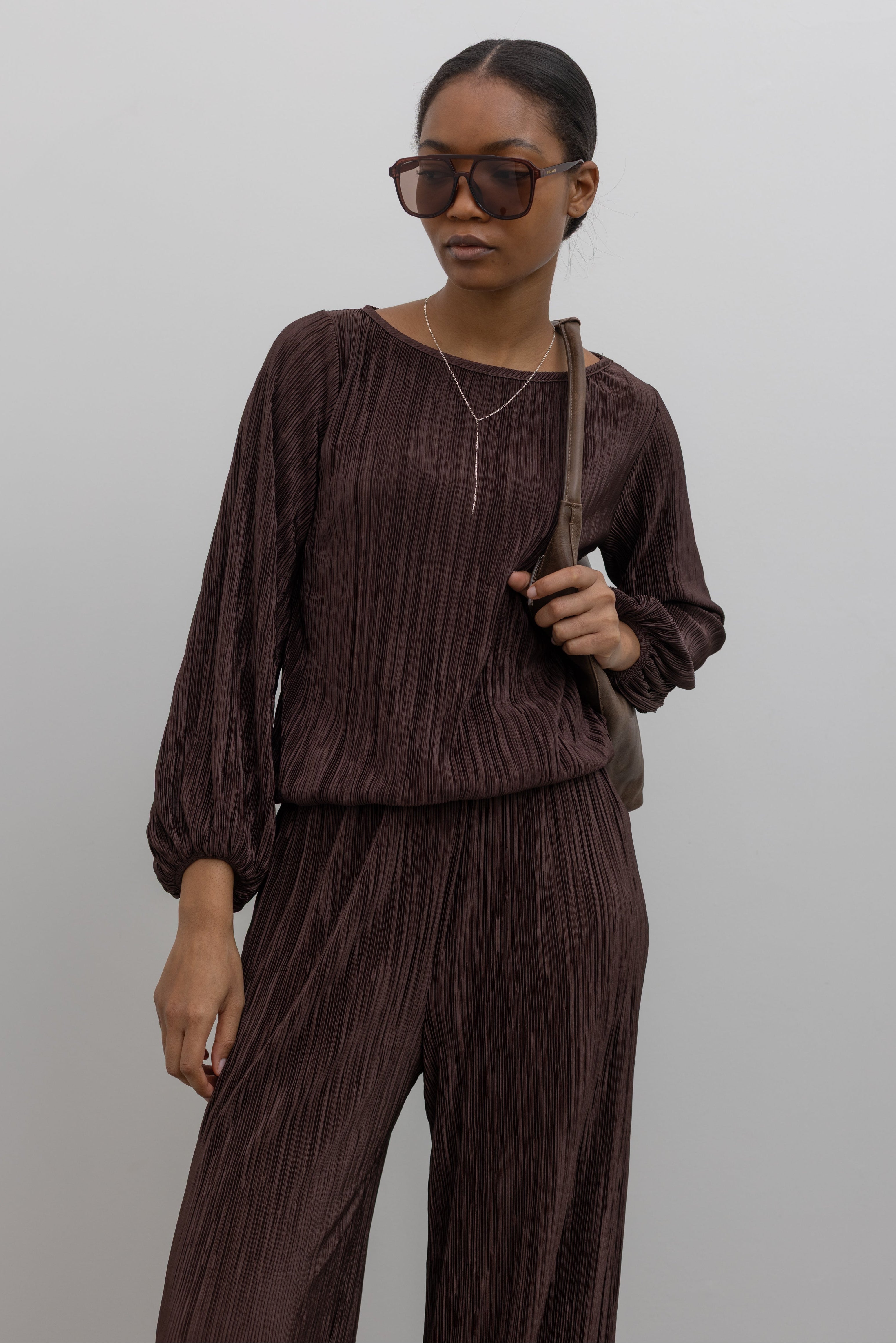Woman wearing a sophisticated chocolate brown plisse long sleeve top with its coordinating pants creating the perfect elevated or casual outfit. 