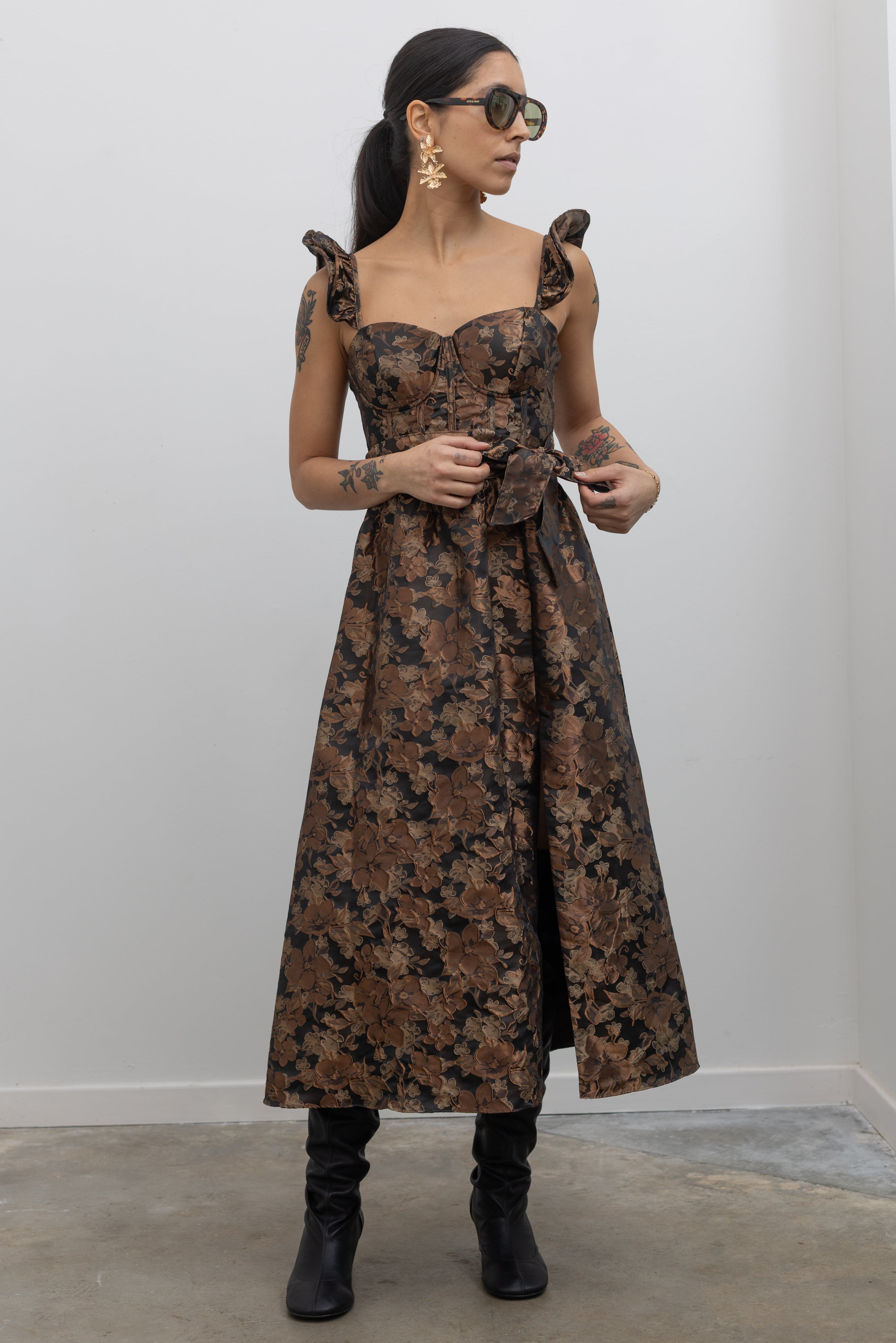 Full front view of a woman wearing flattering feminine Collective label bronze floral jacquard corset midi dress with slouchy black leather heeled boots at Alas Eius. 