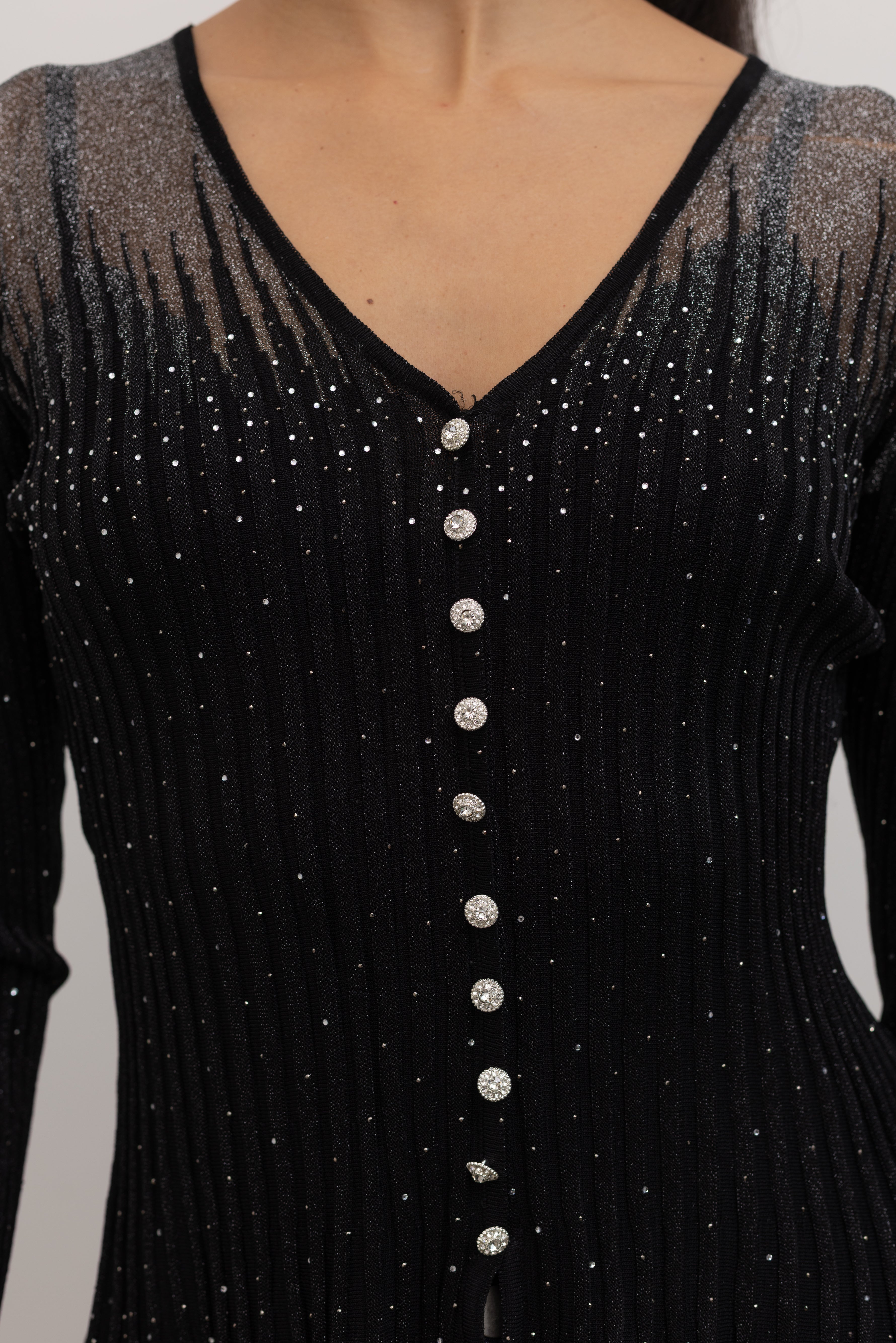 Close-up view of a woman wearing a Collective Label black top featuring a metallic jeweled motif throughout with long bell sleeves and a faux button down front at Alas Eius.