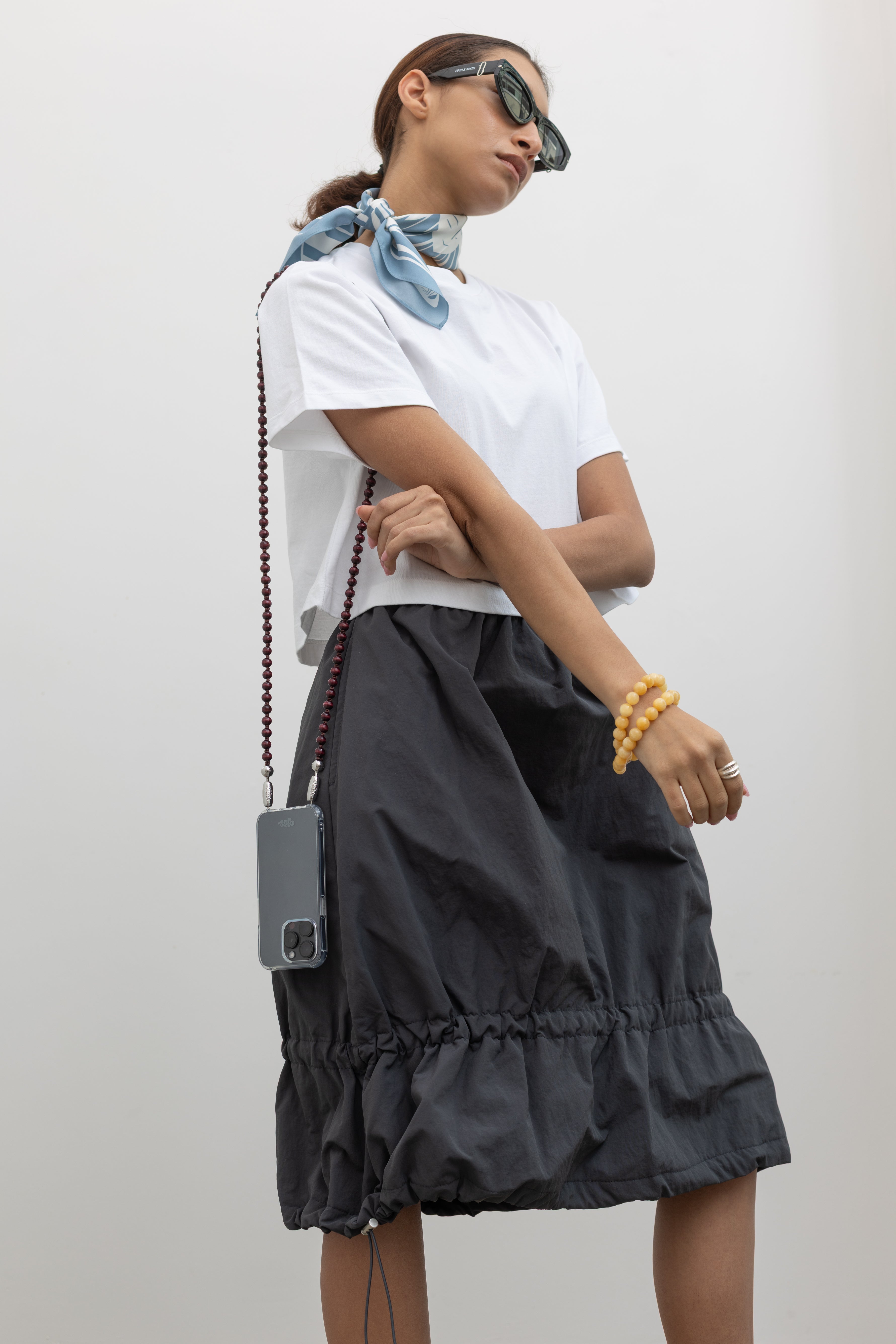 Woman standing wearing Spring fashion in a Collective brand charcoal nylon bungee detail midi skirt with an Alas Eius label cropped white t-shirt at Alas Eius. 