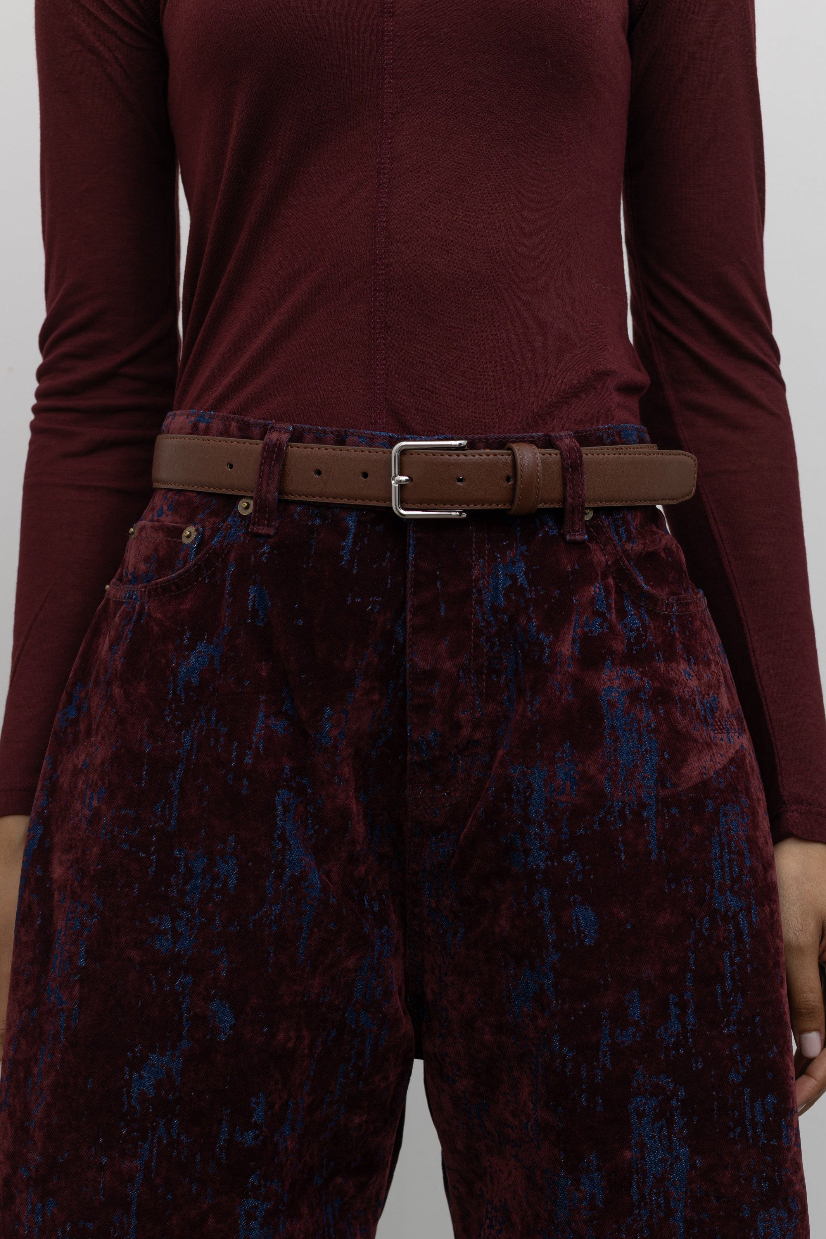 Woman wearing a capsule wardrobe essential accessory in a Collective brand classic brown leather belt made with a silver square shaped buckle at an Alas Eius store. 