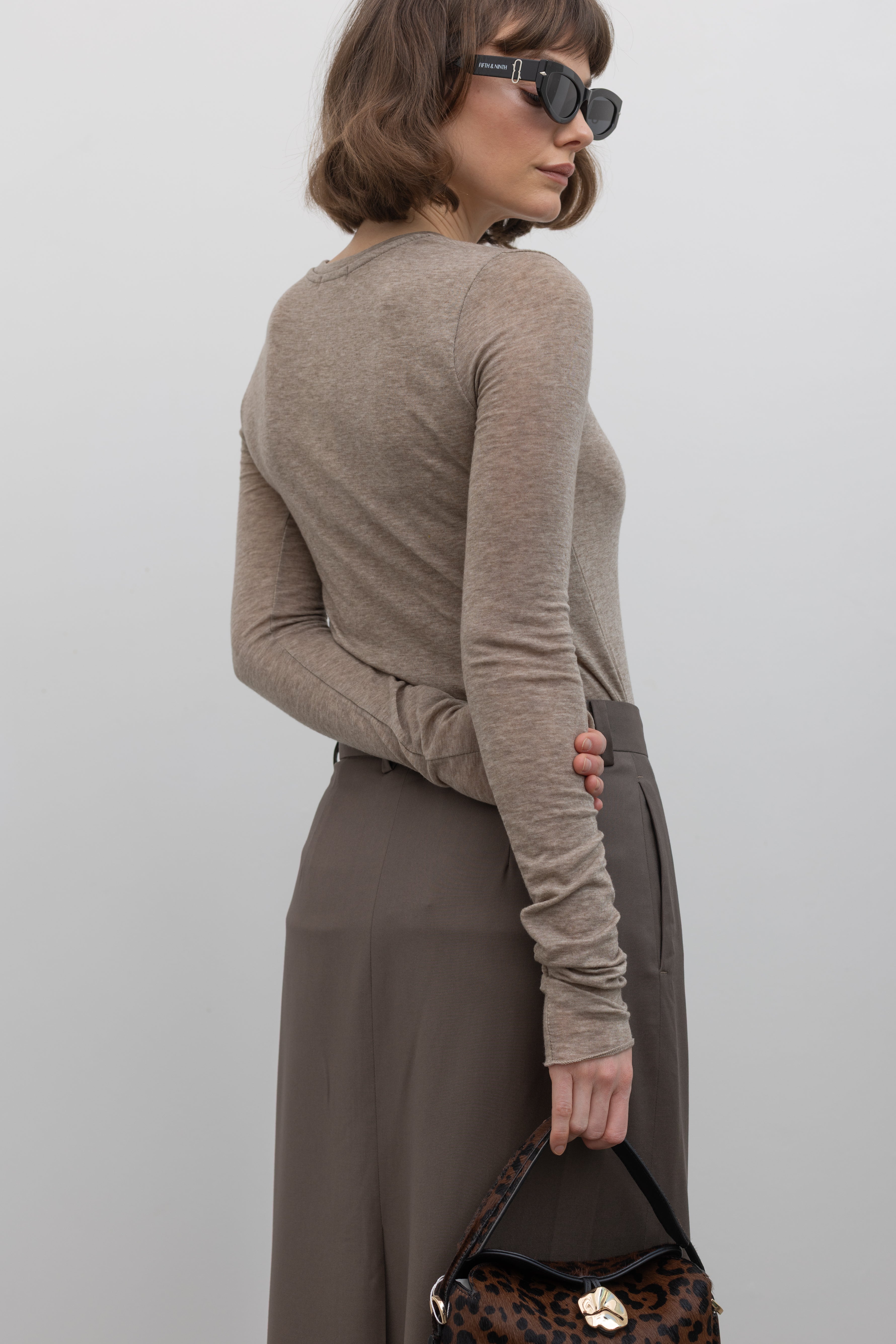 Close-up back view of a woman wearing an elevated capsule wardrobe essential in a Collective Brand Beige Merino Wool Long Sleeve Fitted Top at Alas Eius. 